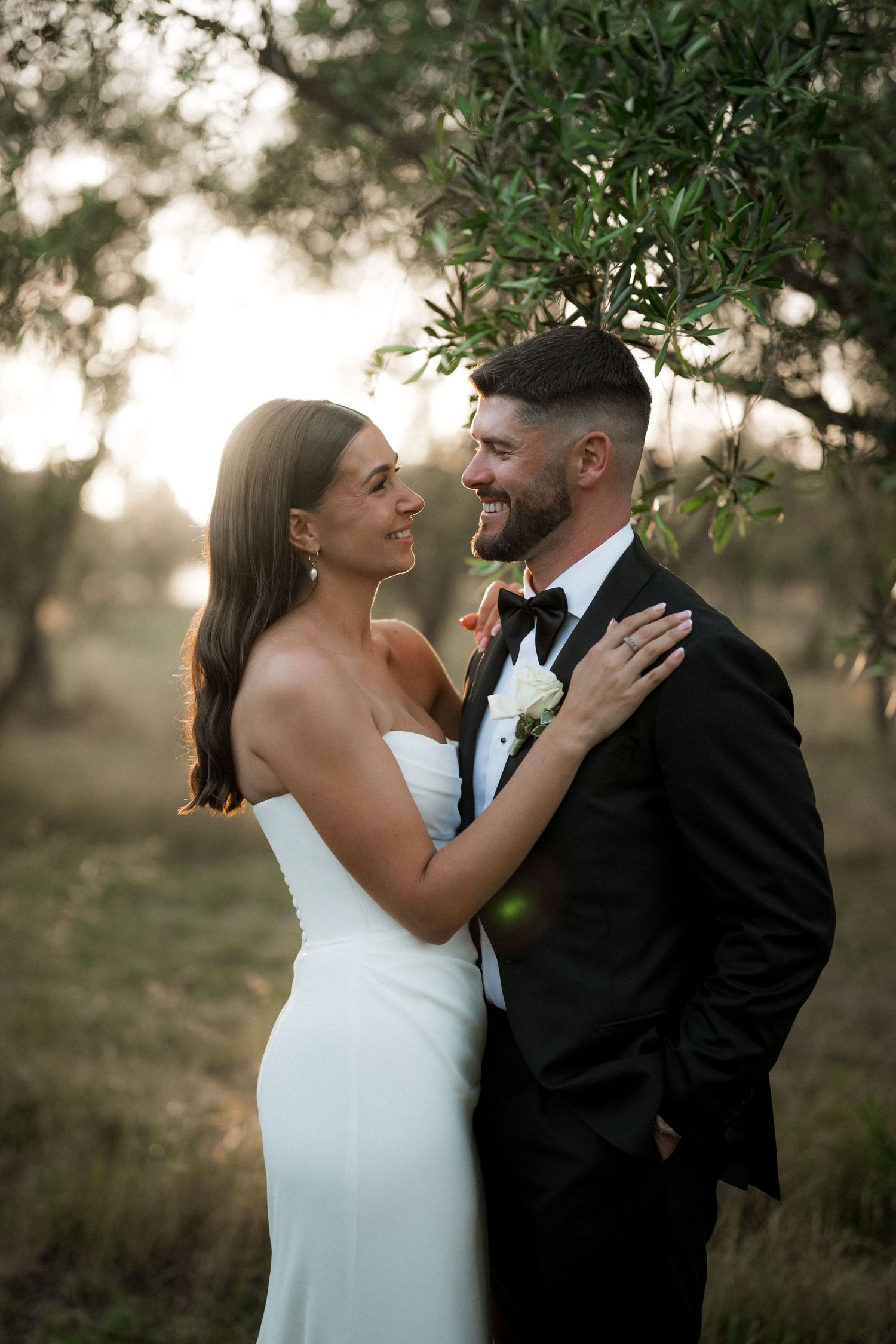 Intimate wedding portrait captured in warm sunset lighting among olive trees.