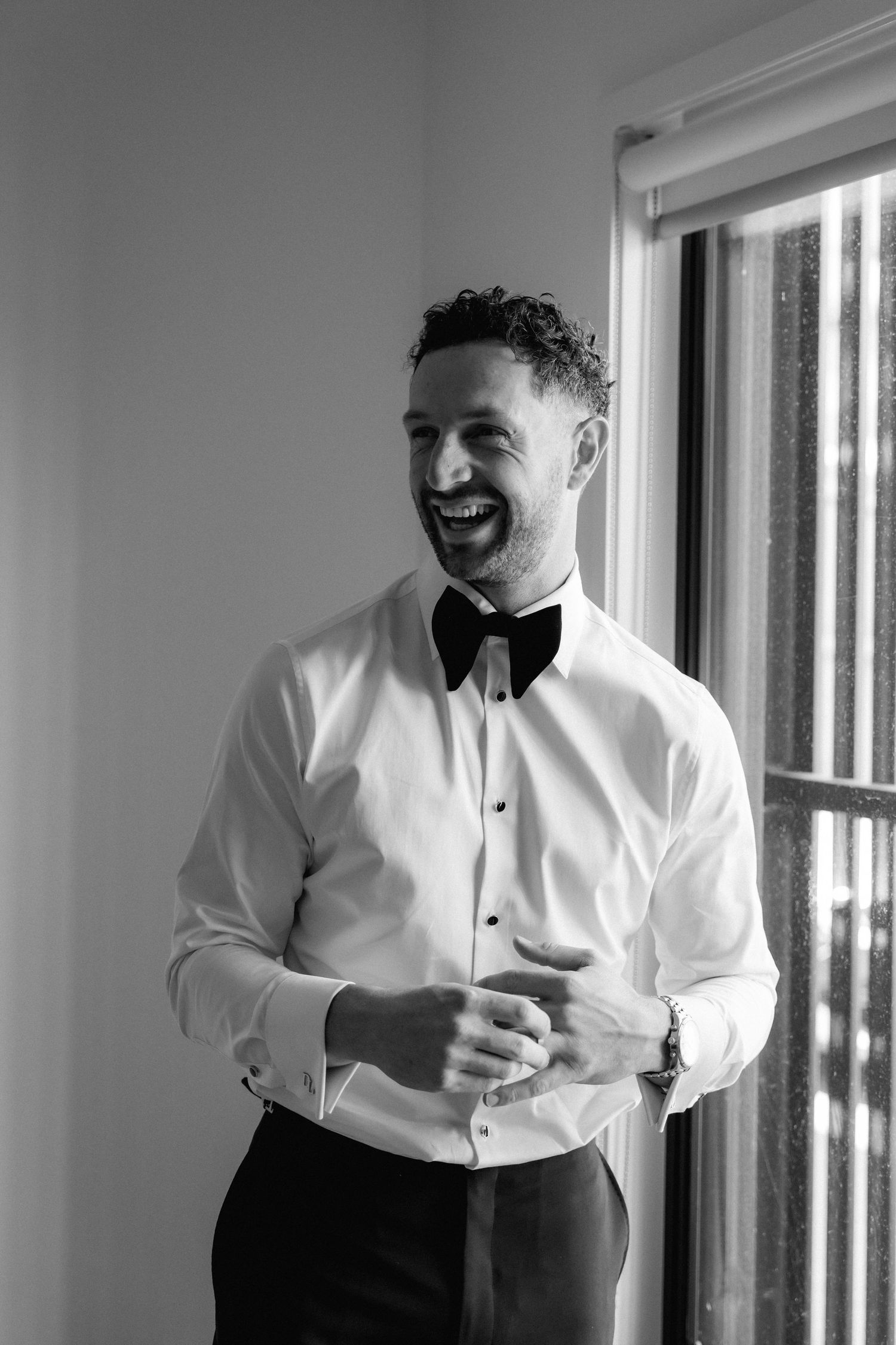 Wedding preparation scene showing groomsmen in white shirts laughing and getting ready.