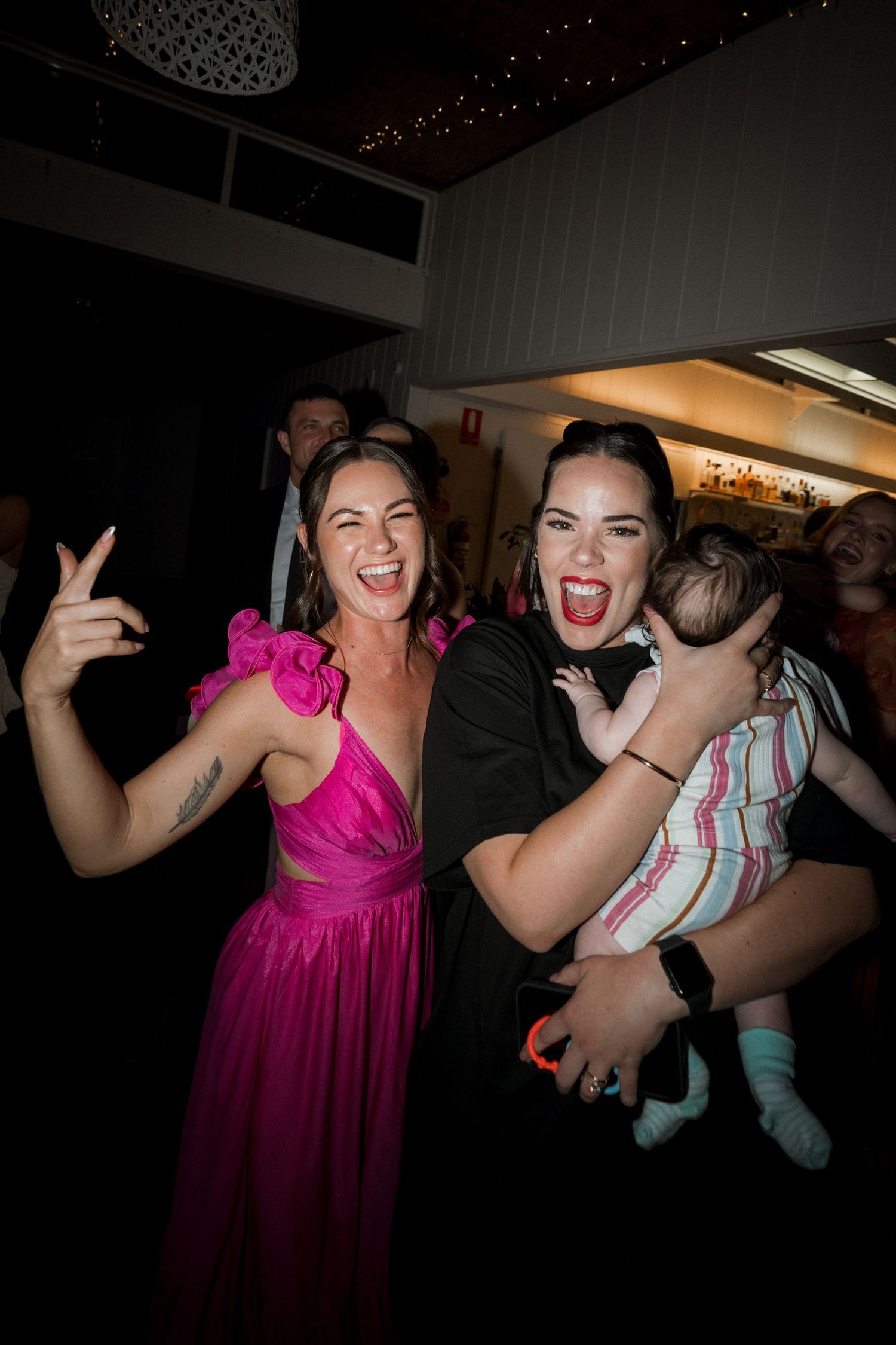Wedding guests dancing and celebrating at a reception with festive lighting.