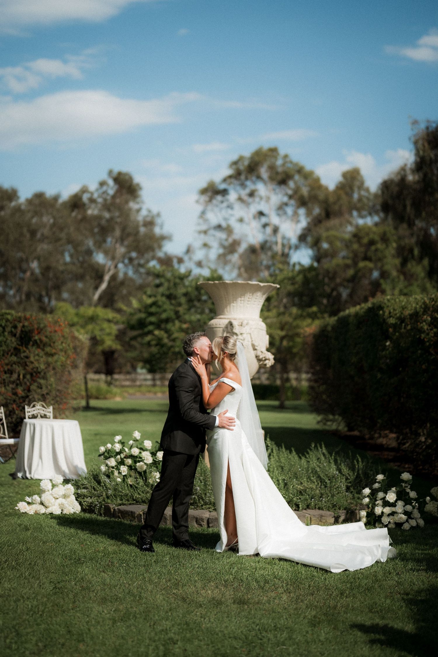 A romantic wedding moment captured in a lush garden setting with white floral decorations.