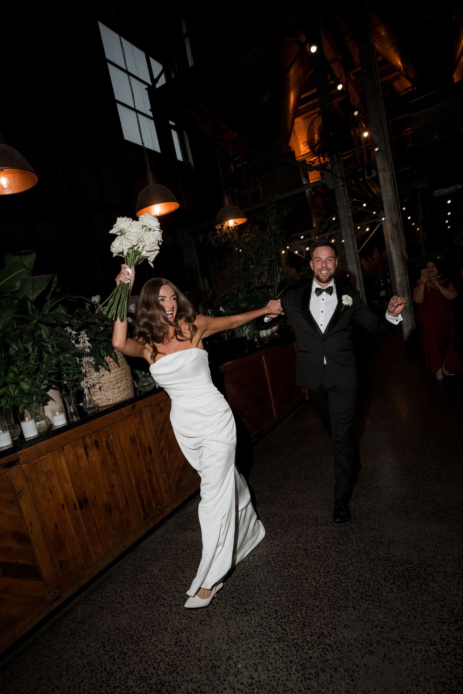 A couple dances and celebrates at their wedding reception in a dimly lit venue with wooden planters.