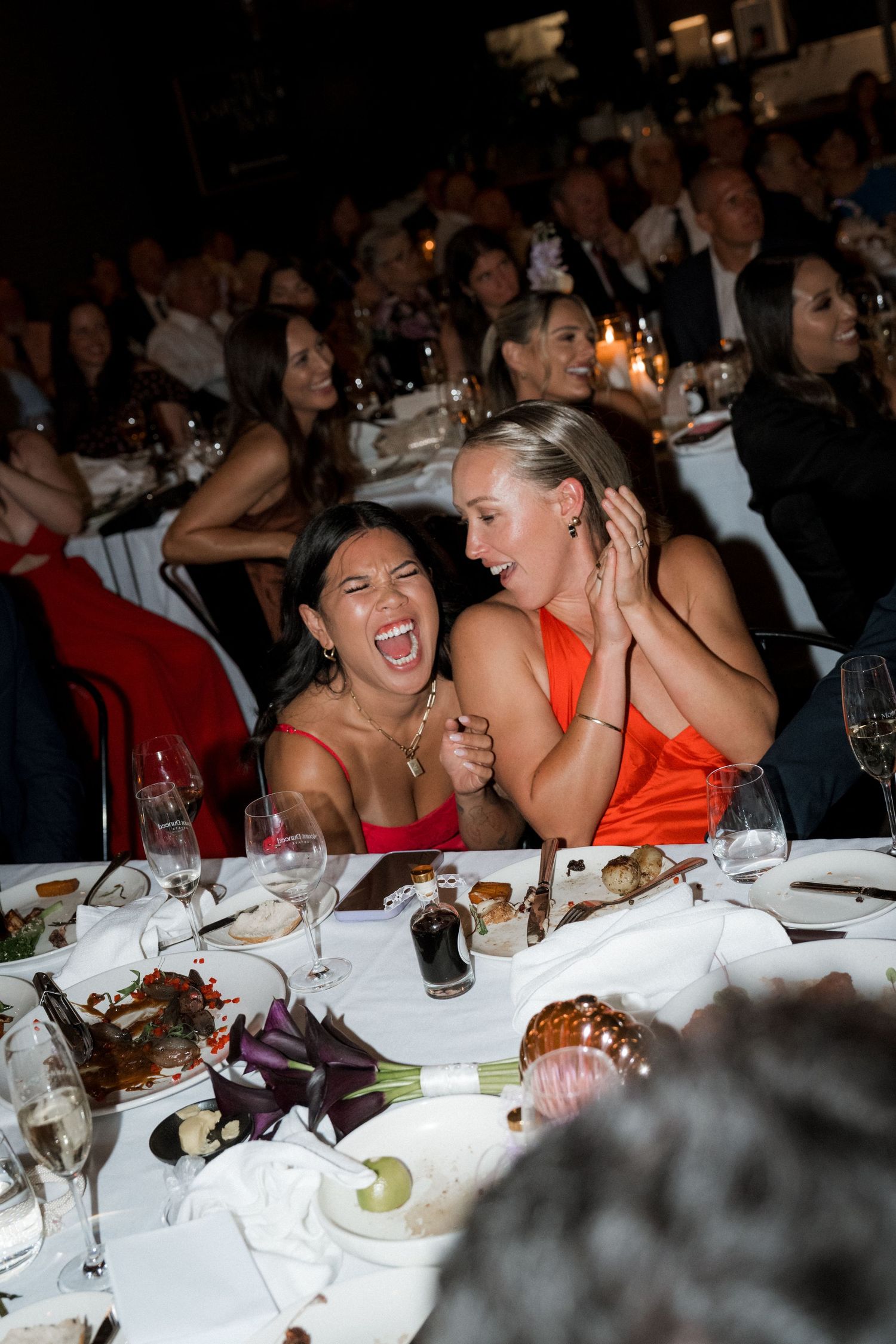 Wedding reception guests laughing and enjoying dinner at a formal table setting.