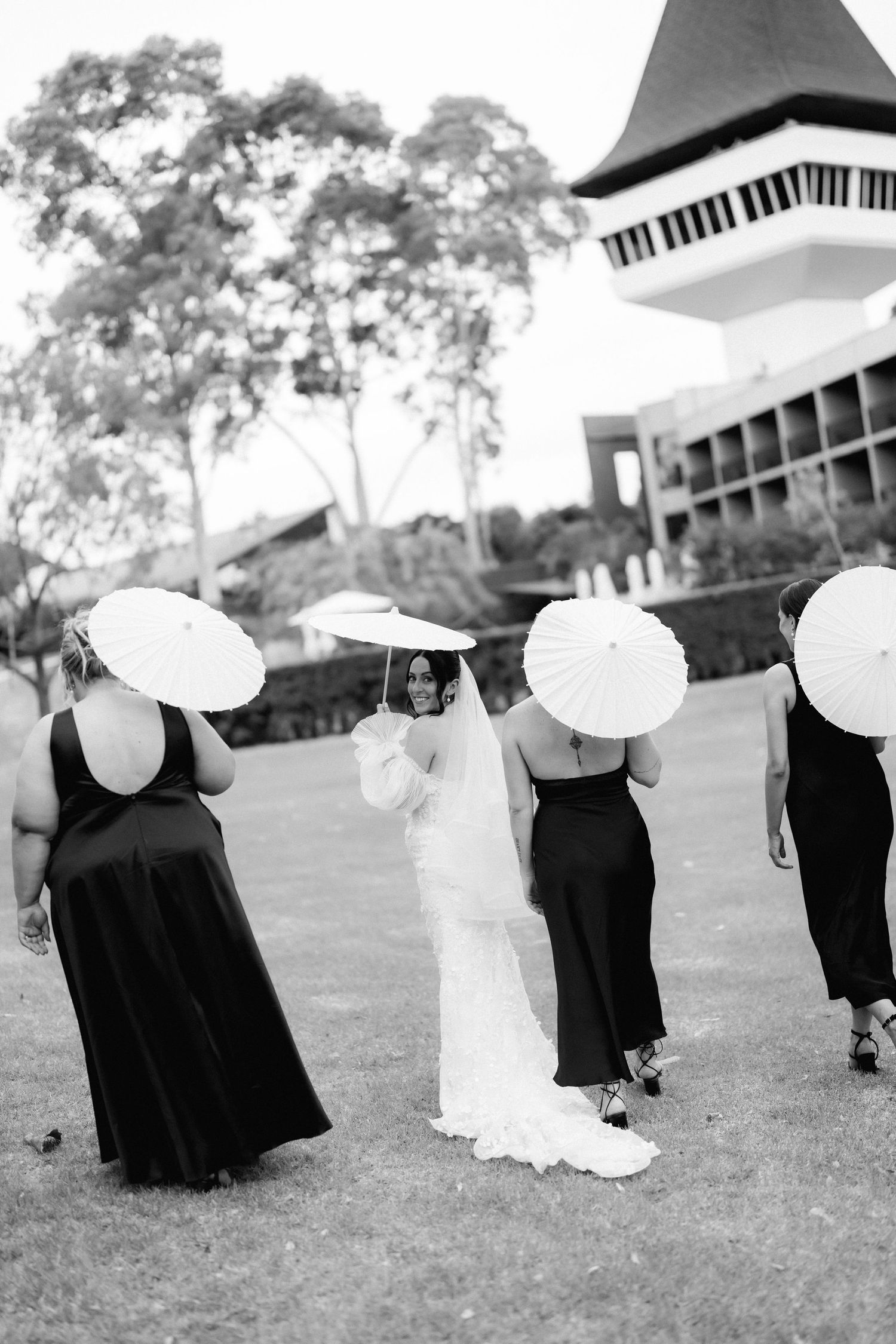 Wedding party in formal attire lined up on grass with a building in background.