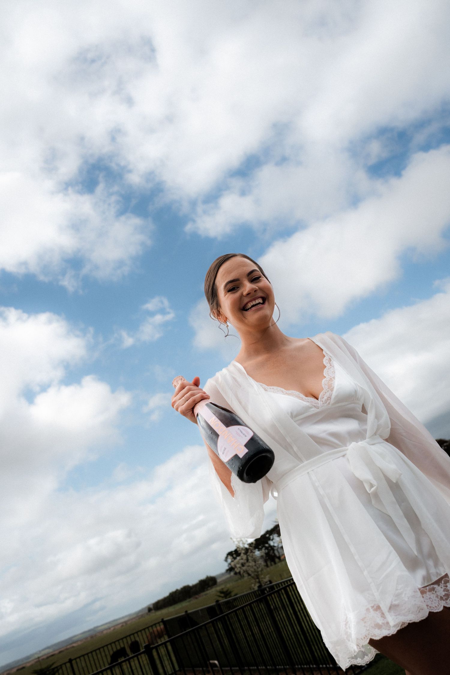 A person in a white dress twirls joyfully against a blue sky with clouds on a sunny day.