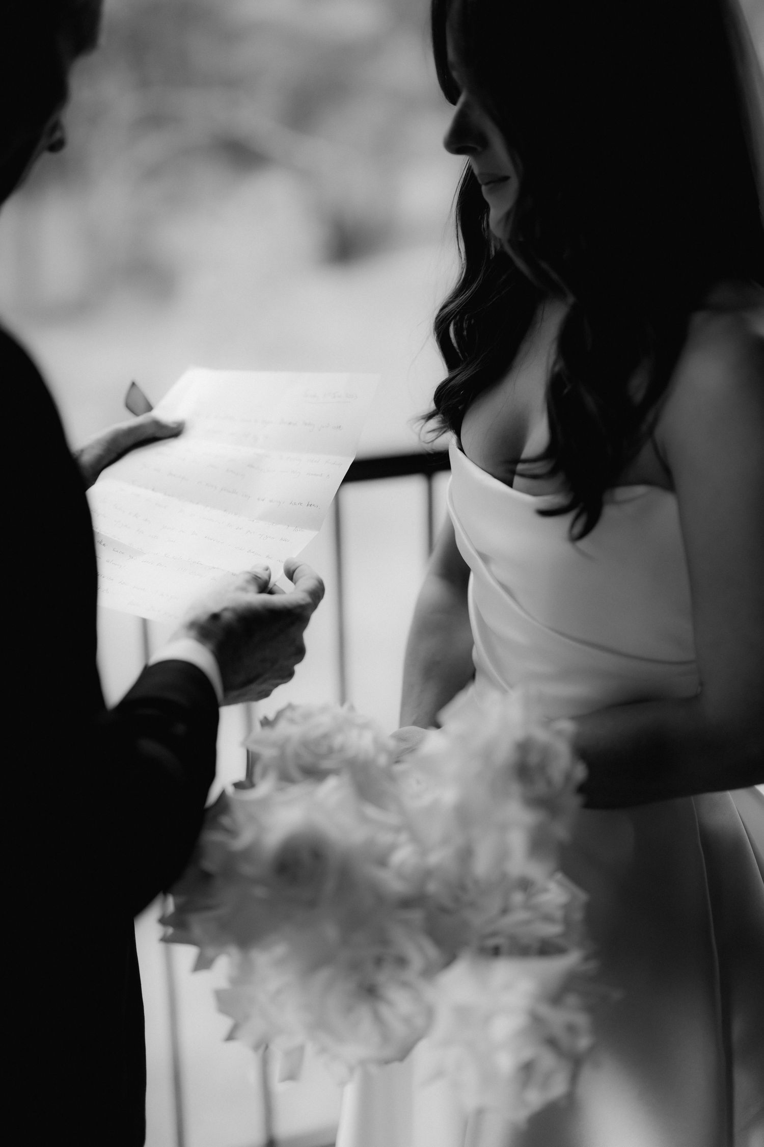 Black and white image of a couple exchanging vows with a white bouquet in frame.
