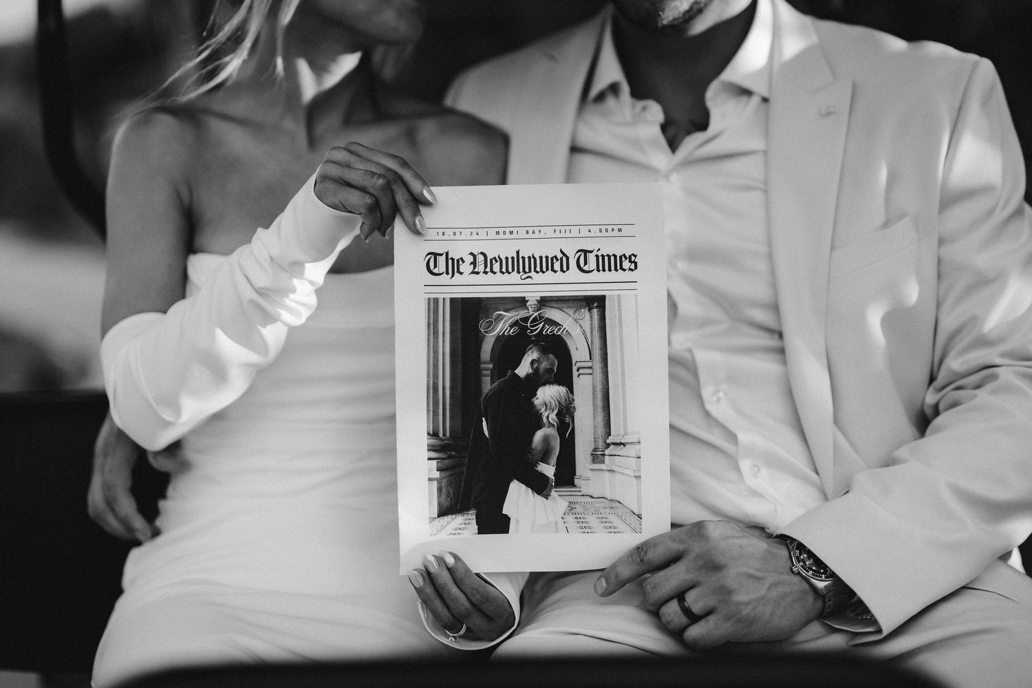A couple in wedding attire holding up a black and white newspaper clipping.