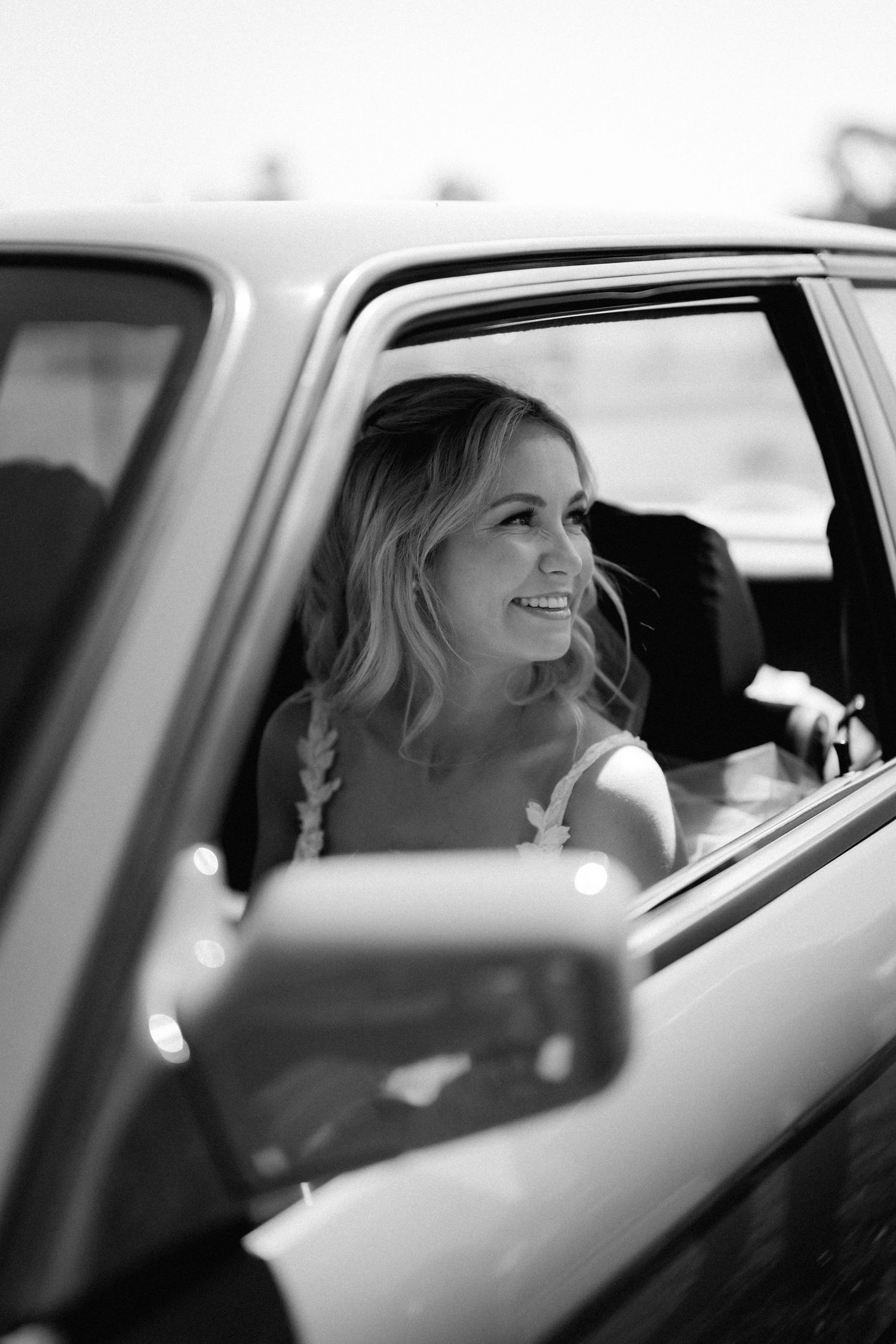 Black and white portrait of bride smiling through car window.