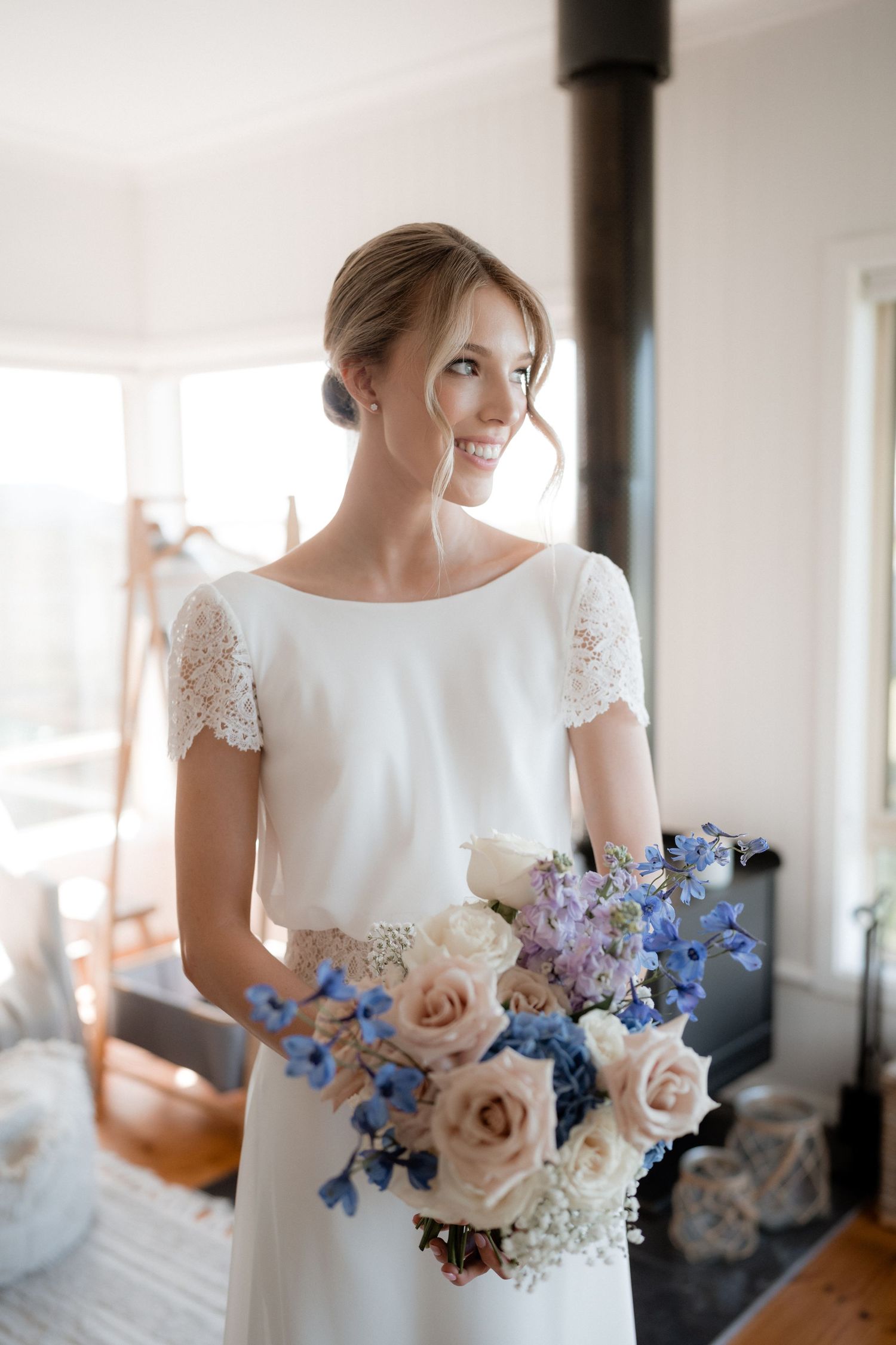 Elegant bridal portrait featuring a lace-sleeved dress and bouquet with blue and pink flowers.