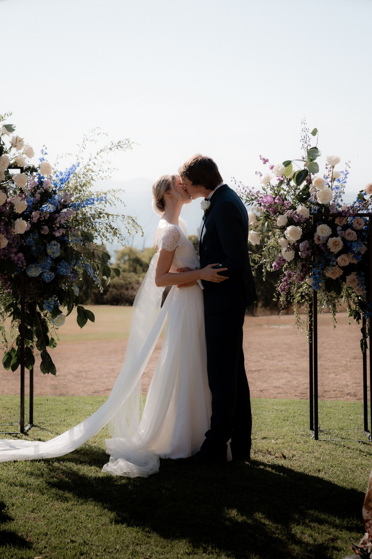 A romantic wedding ceremony under floral arches with delicate blue and white blooms in an outdoor garden setting.