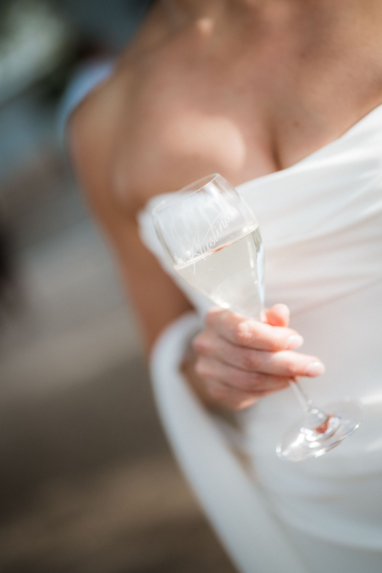 Close-up detail of champagne glass held against white wedding dress.