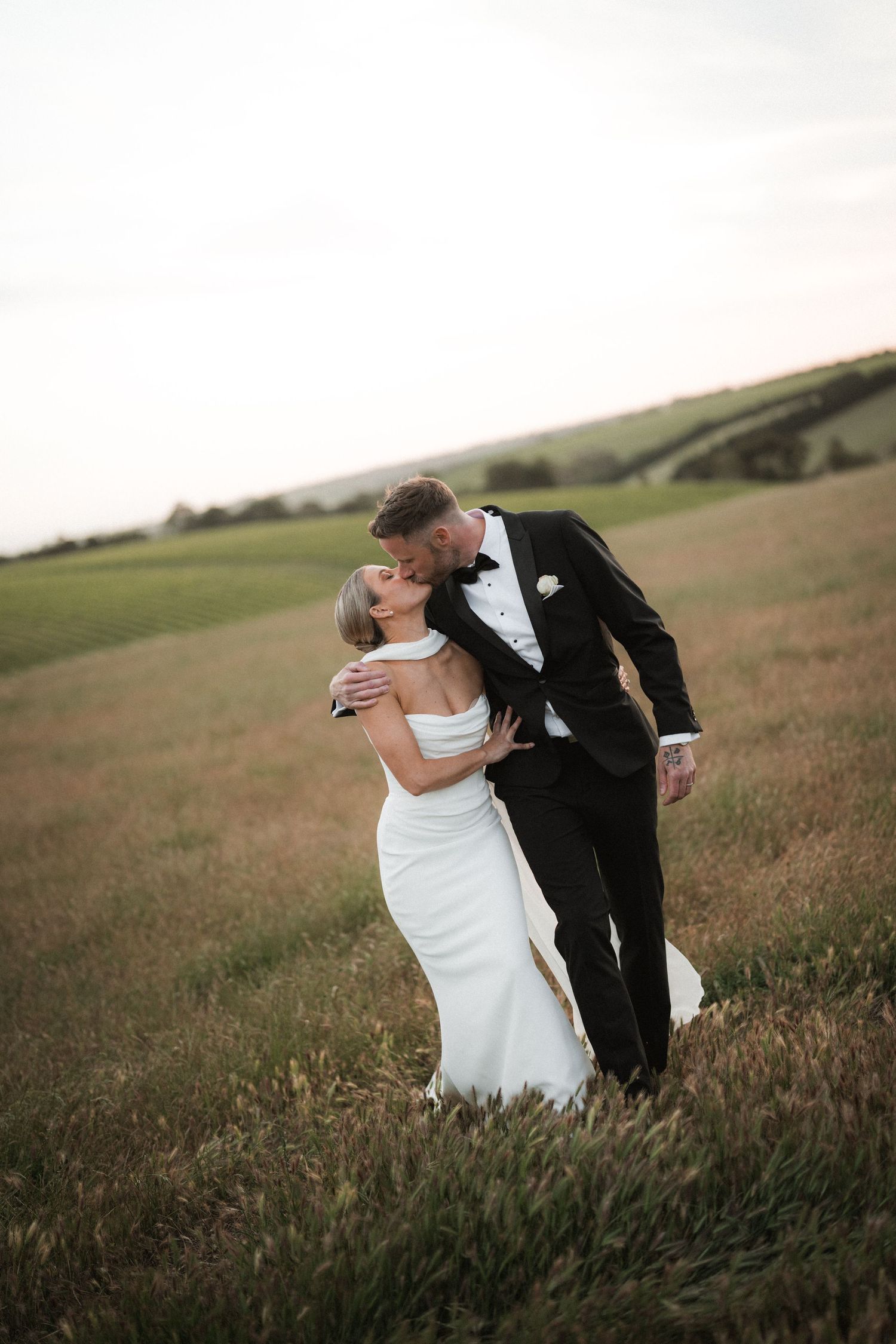 A romantic dip pose between newlyweds in an open field during golden hour.