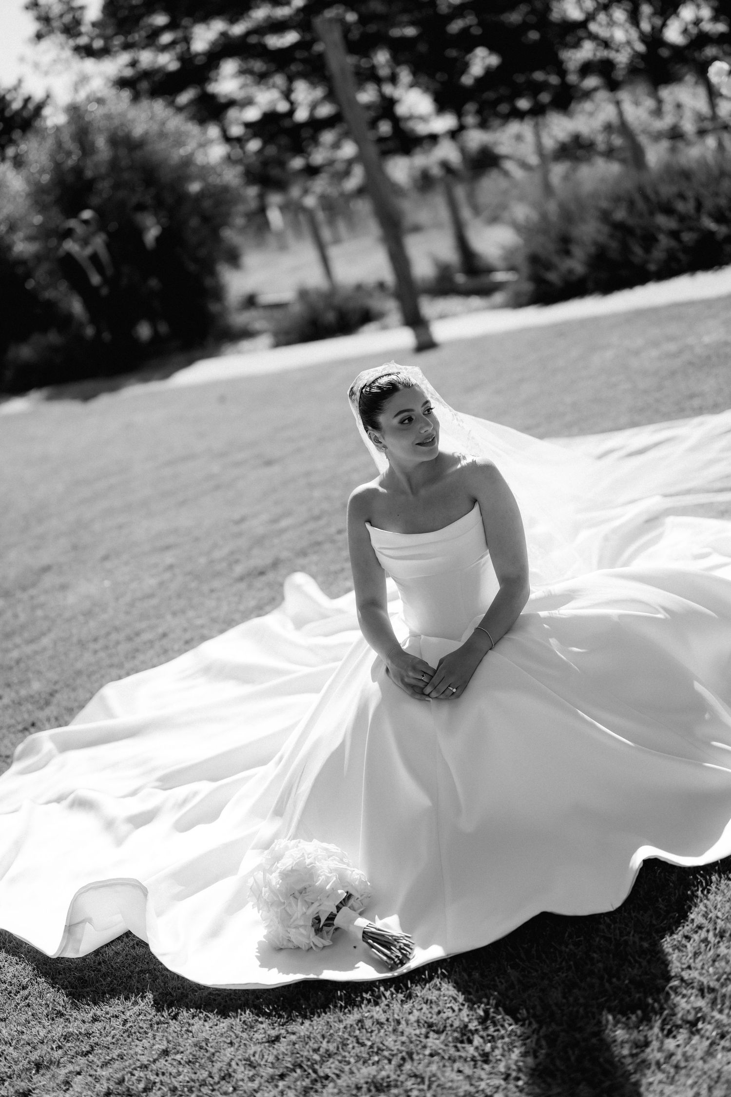 Bride in flowing white gown poses gracefully on grass in black and white photography.