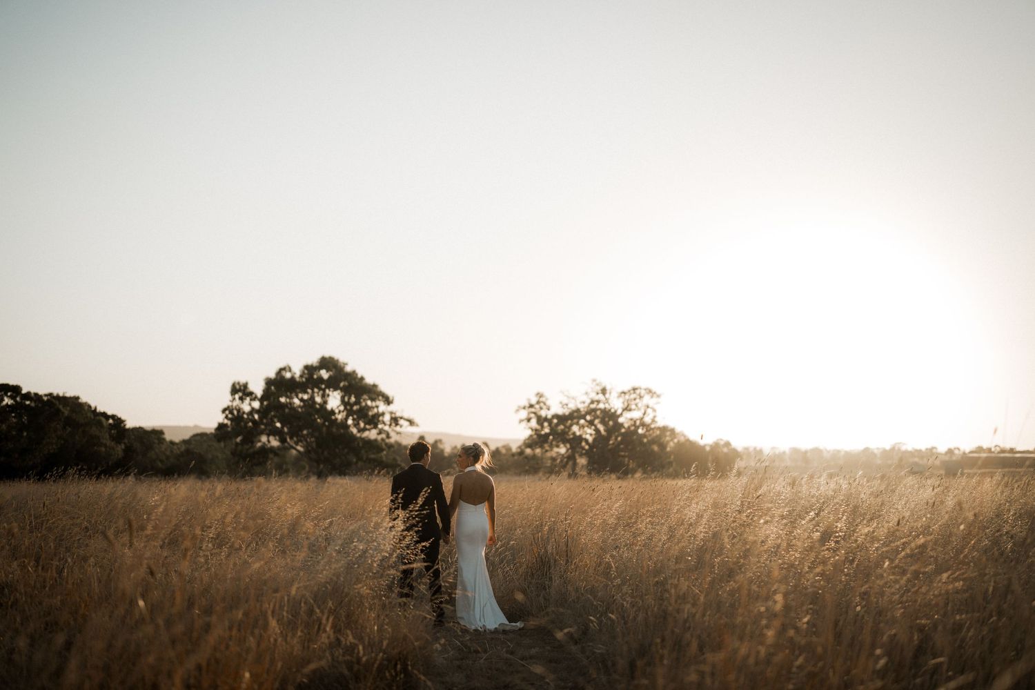 Silhouetted couple walking through tall grass field at sunset.