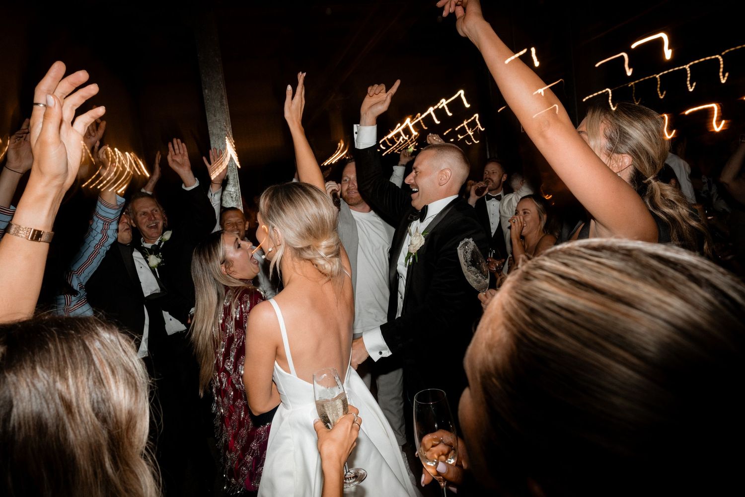 Wedding reception guests with raised arms dancing enthusiastically on a crowded dance floor.