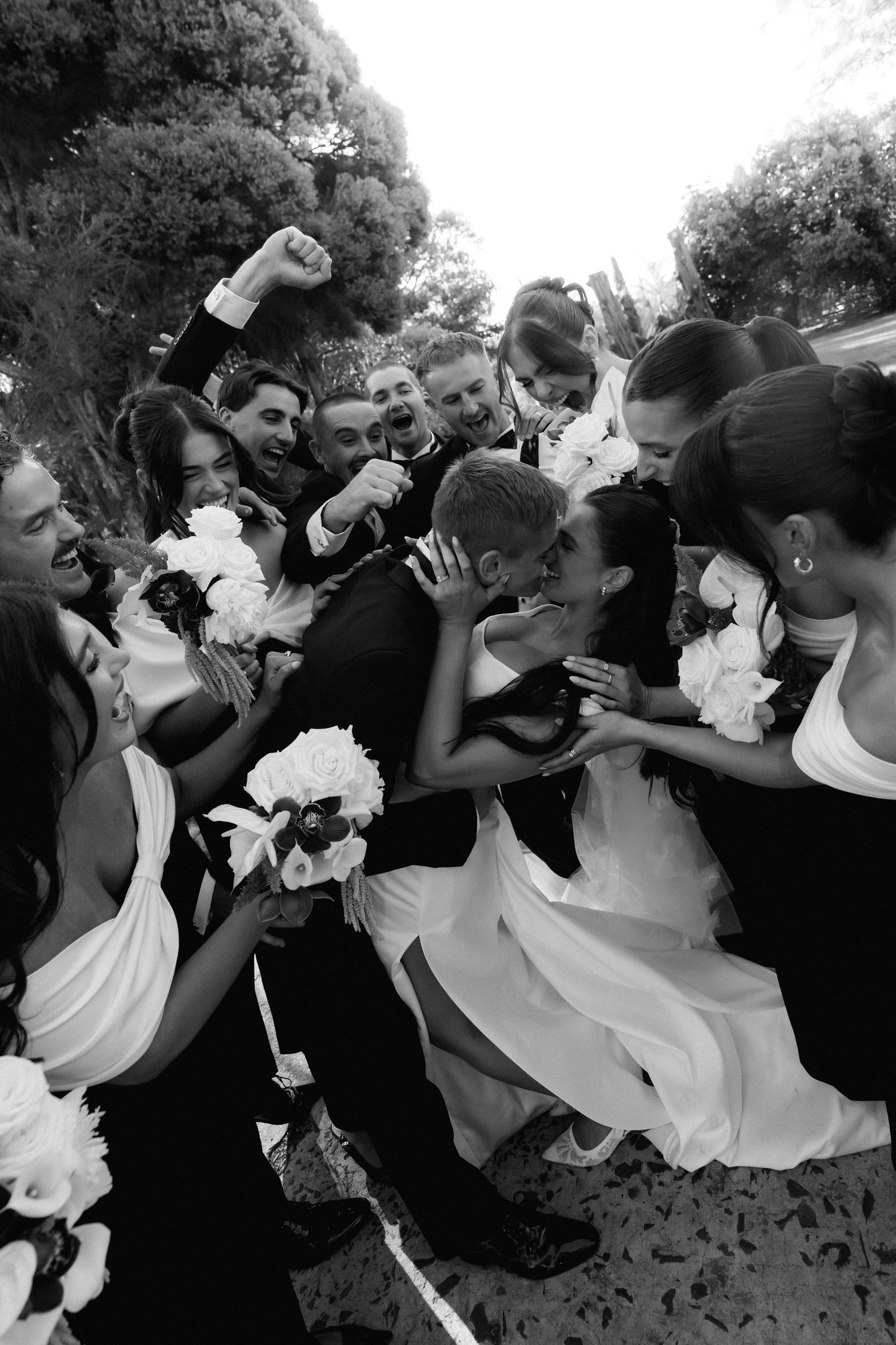 Wedding party celebrates with joyful group pose in black and white photo showing bridesmaids and groomsmen.