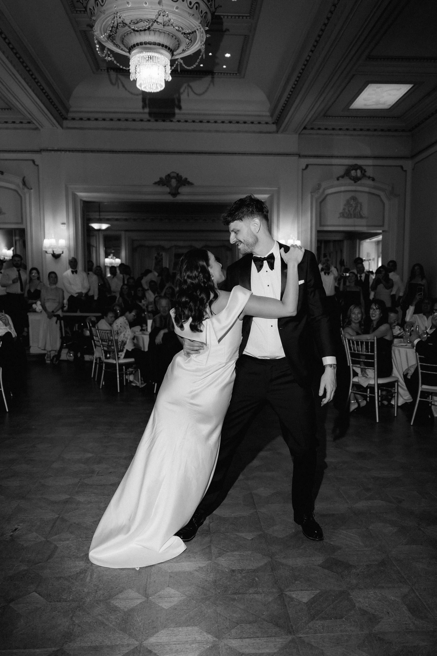 A couple dances dramatically at a wedding reception in an elegant ballroom featuring ornate chandeliers and decor.