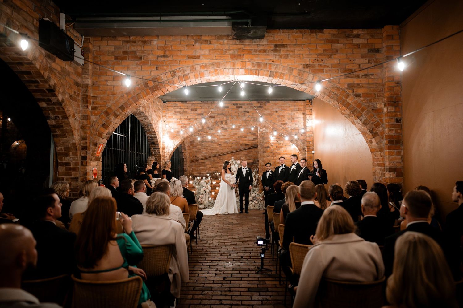 Wedding ceremony in historic brick archway venue with guests seated in rows.