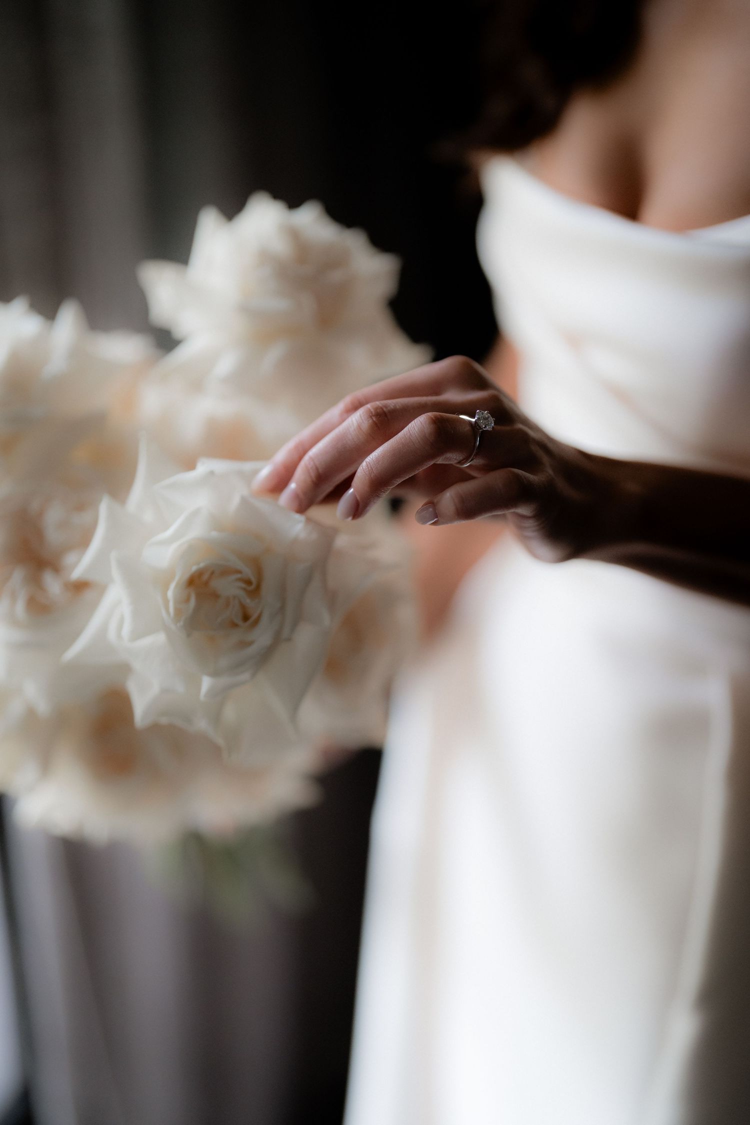 Close-up of diamond ring with white roses and wedding dress fabric.