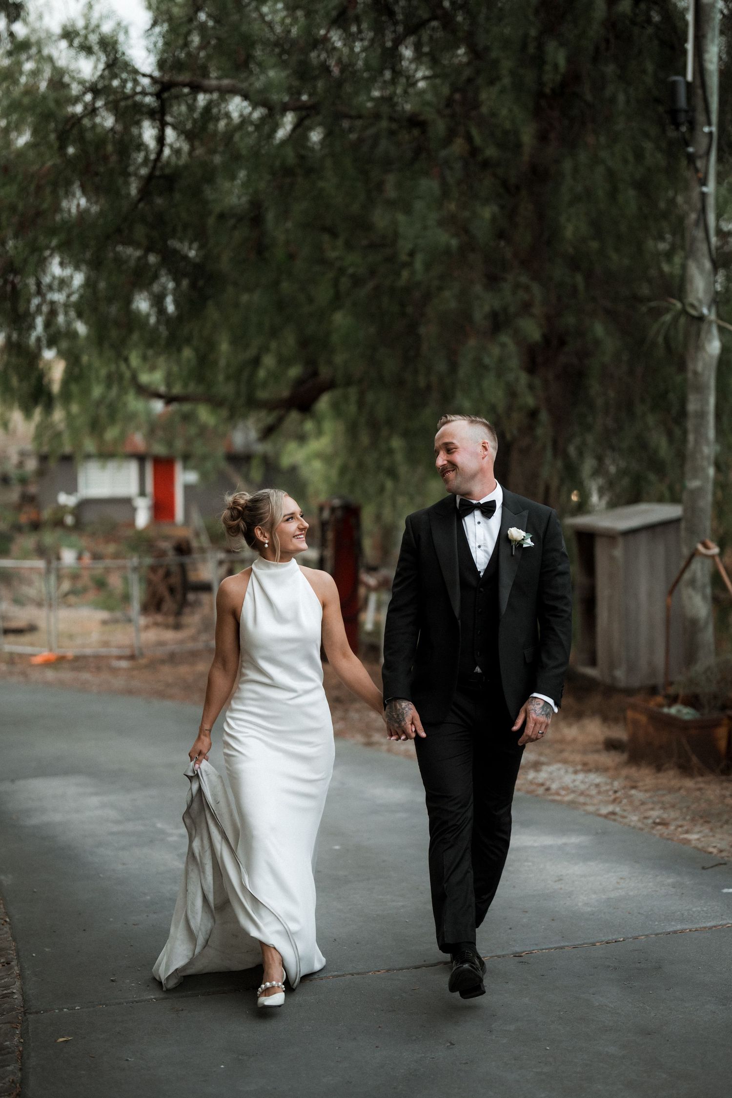 A bride and groom walk together on a path surrounded by trees during their outdoor wedding shoot.