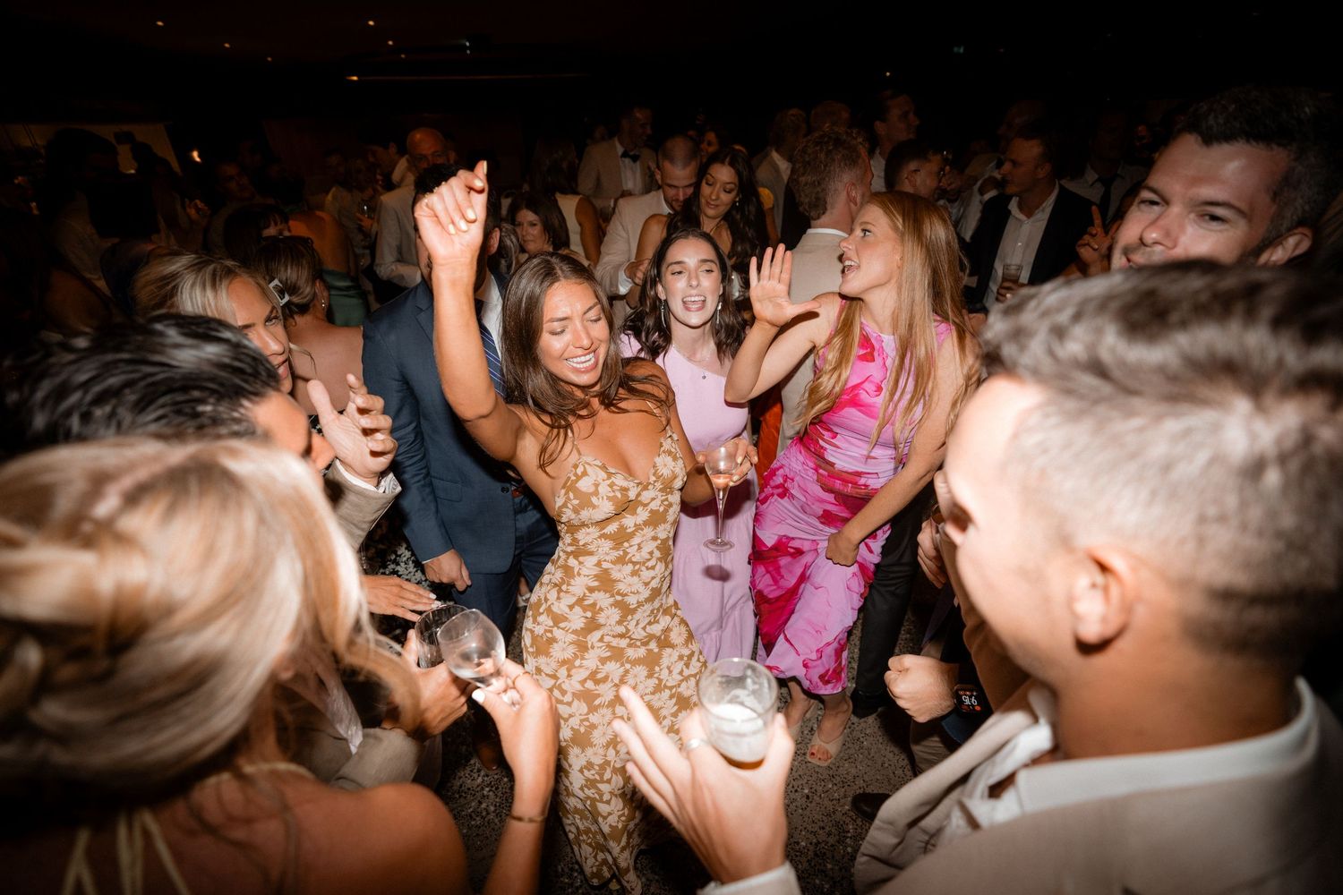 Energetic crowd of party guests dancing and celebrating on a crowded dance floor at a nighttime event.