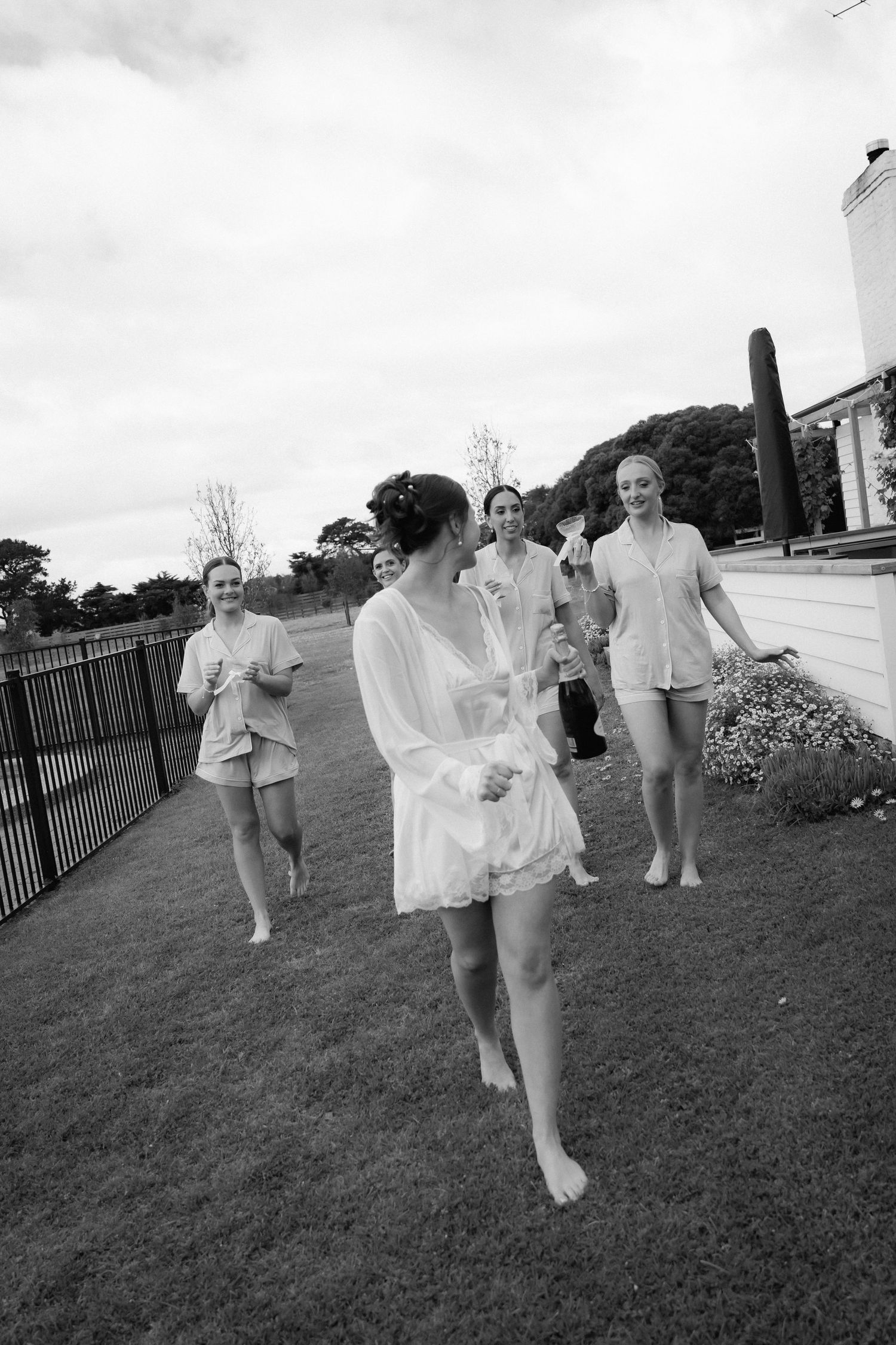 A group in white attire runs playfully across a grassy lawn during an outdoor celebration.