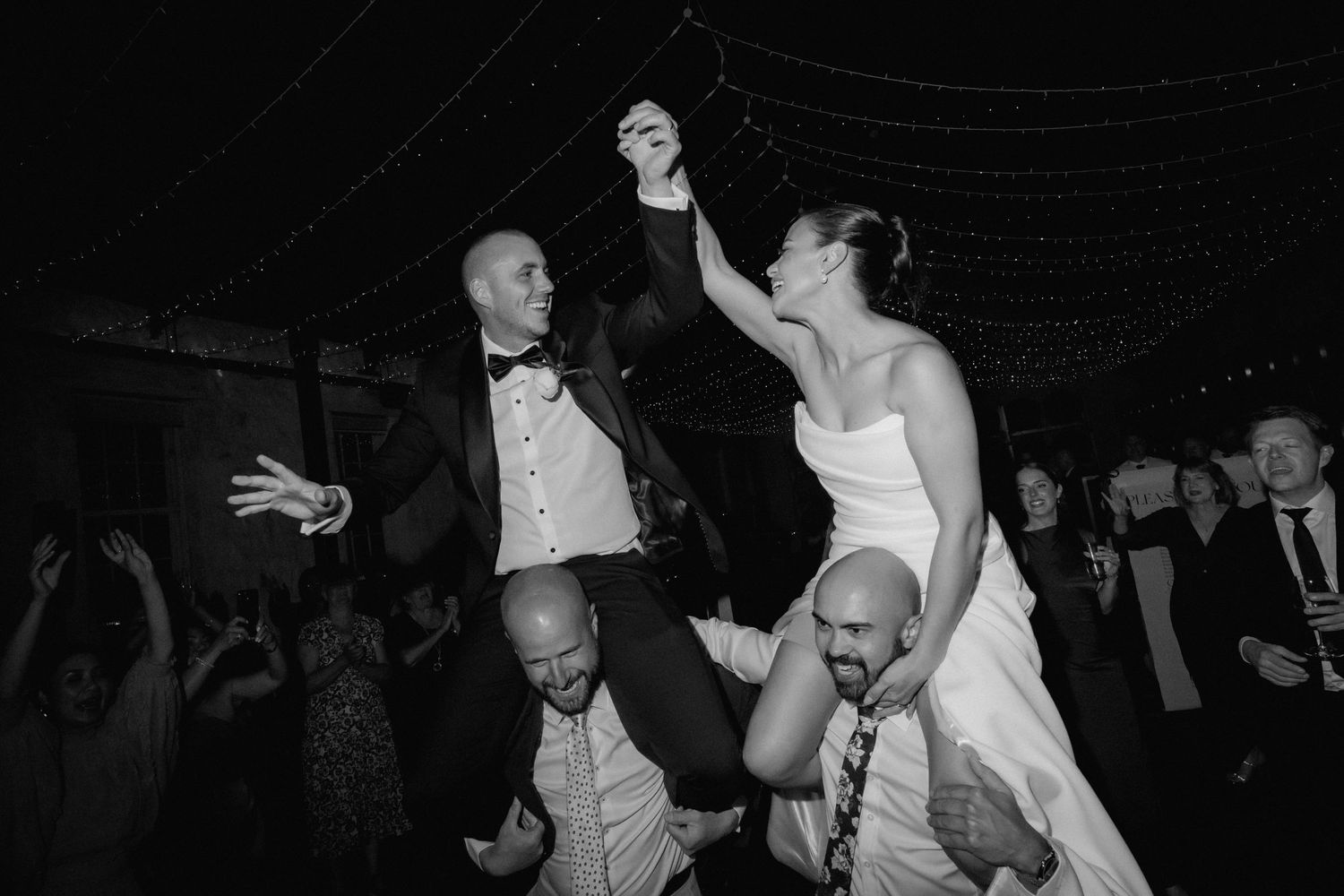 Black and white photo captures energetic dance floor celebration at wedding reception.