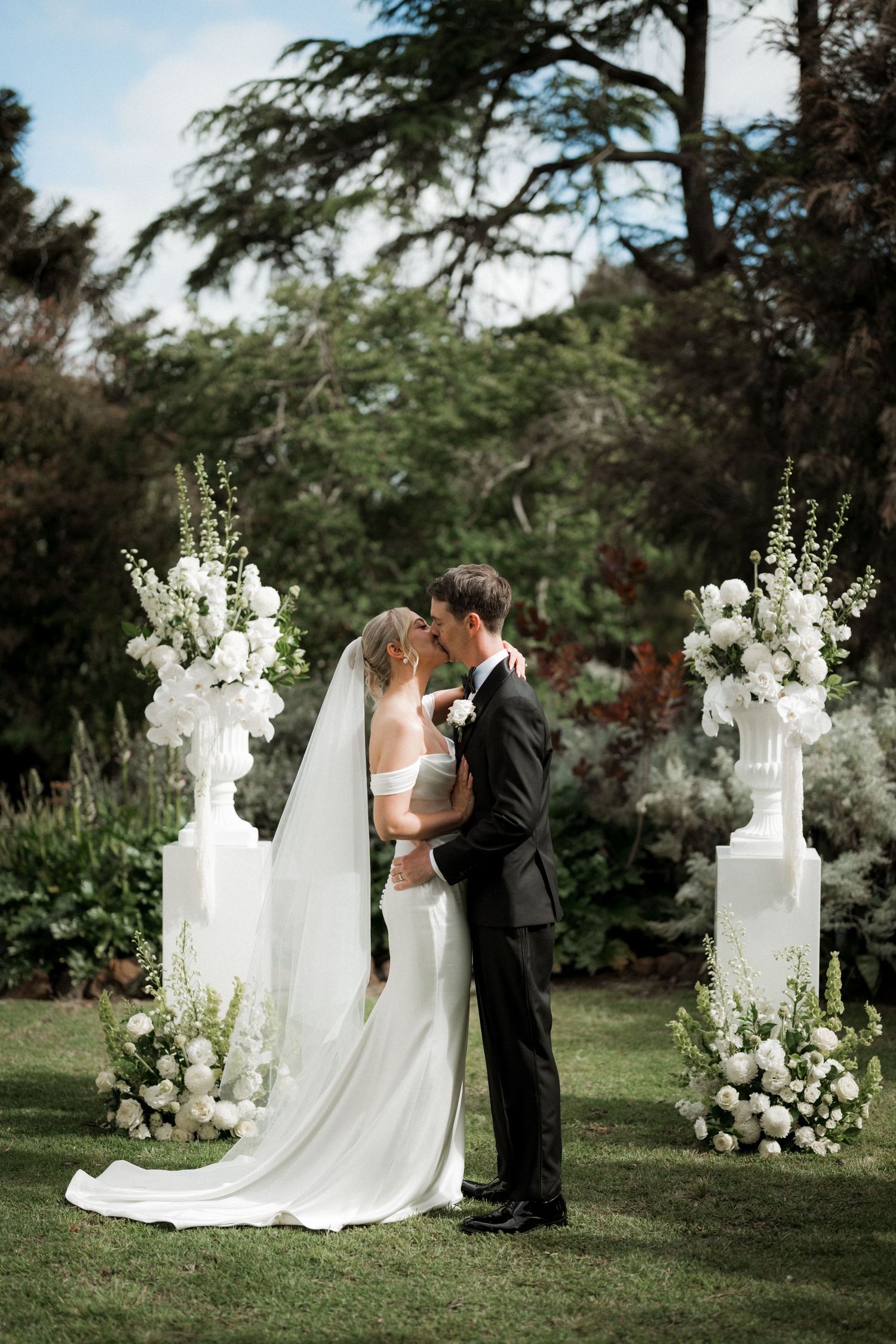 Outdoor wedding ceremony setup with white floral arrangements and a couple sharing an intimate moment.