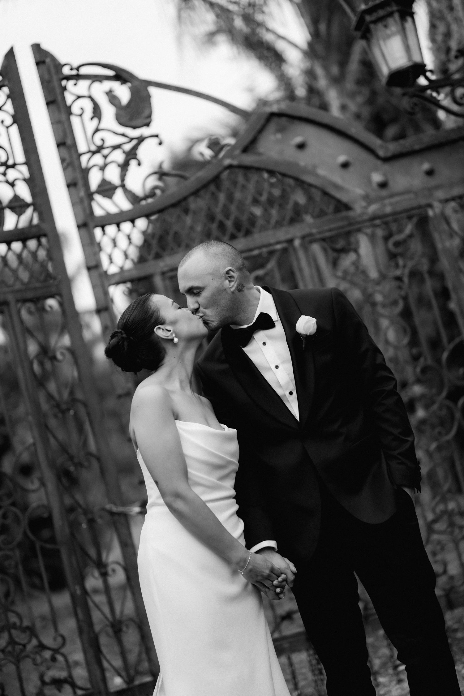 A romantic black and white wedding photo series showing a couple sharing intimate kisses in an ornate outdoor setting.