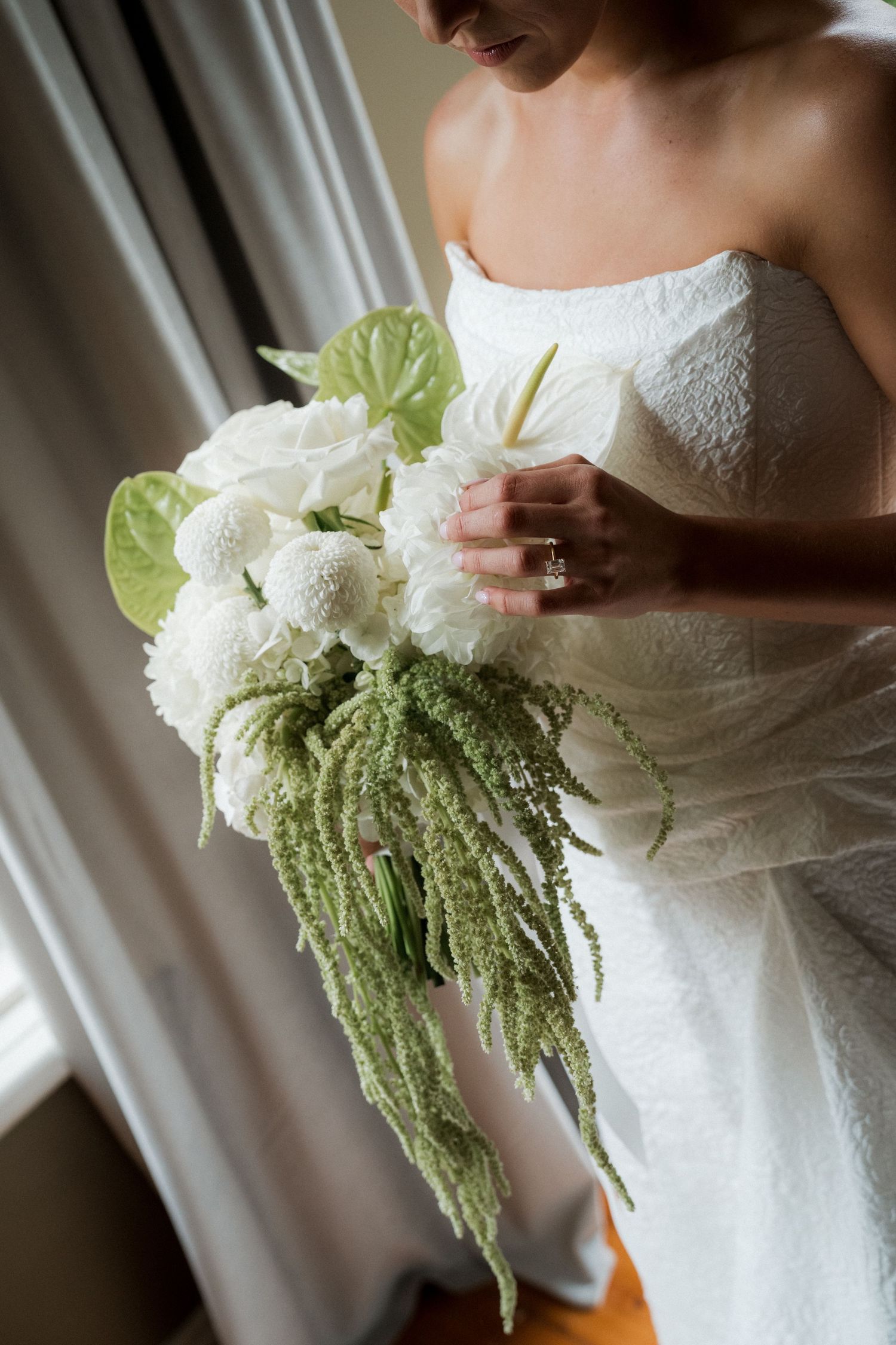 Close-up of bride in strapless gown holding white bouquet with cascading green amaranthus.