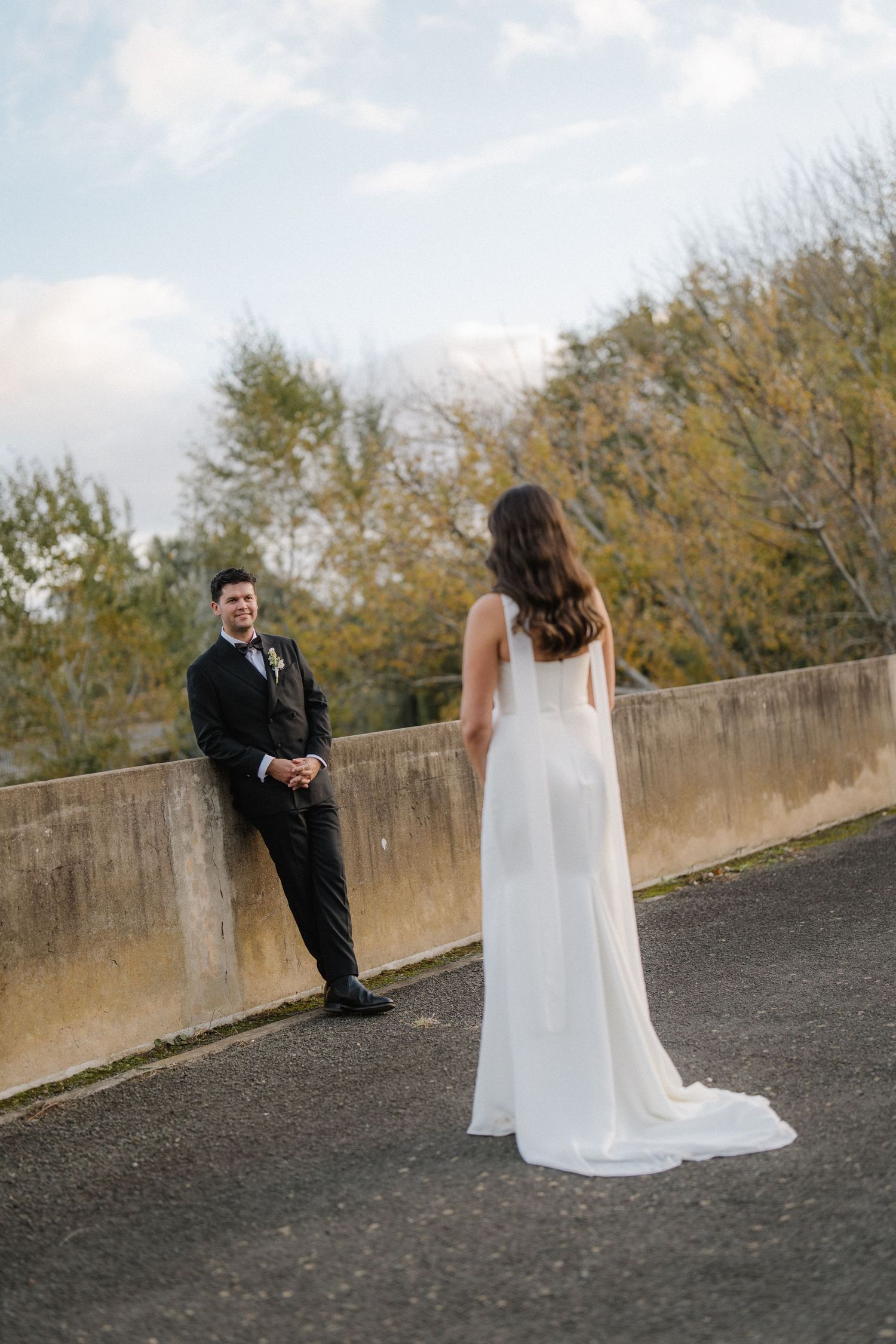 Wedding couple sharing a moment on a concrete wall with autumn trees in the background.