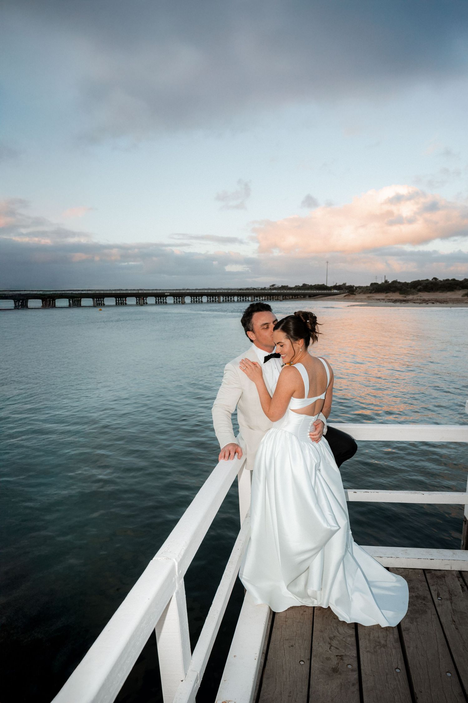 Romantic wedding photos on a wooden pier with ocean and sunset views in the background.