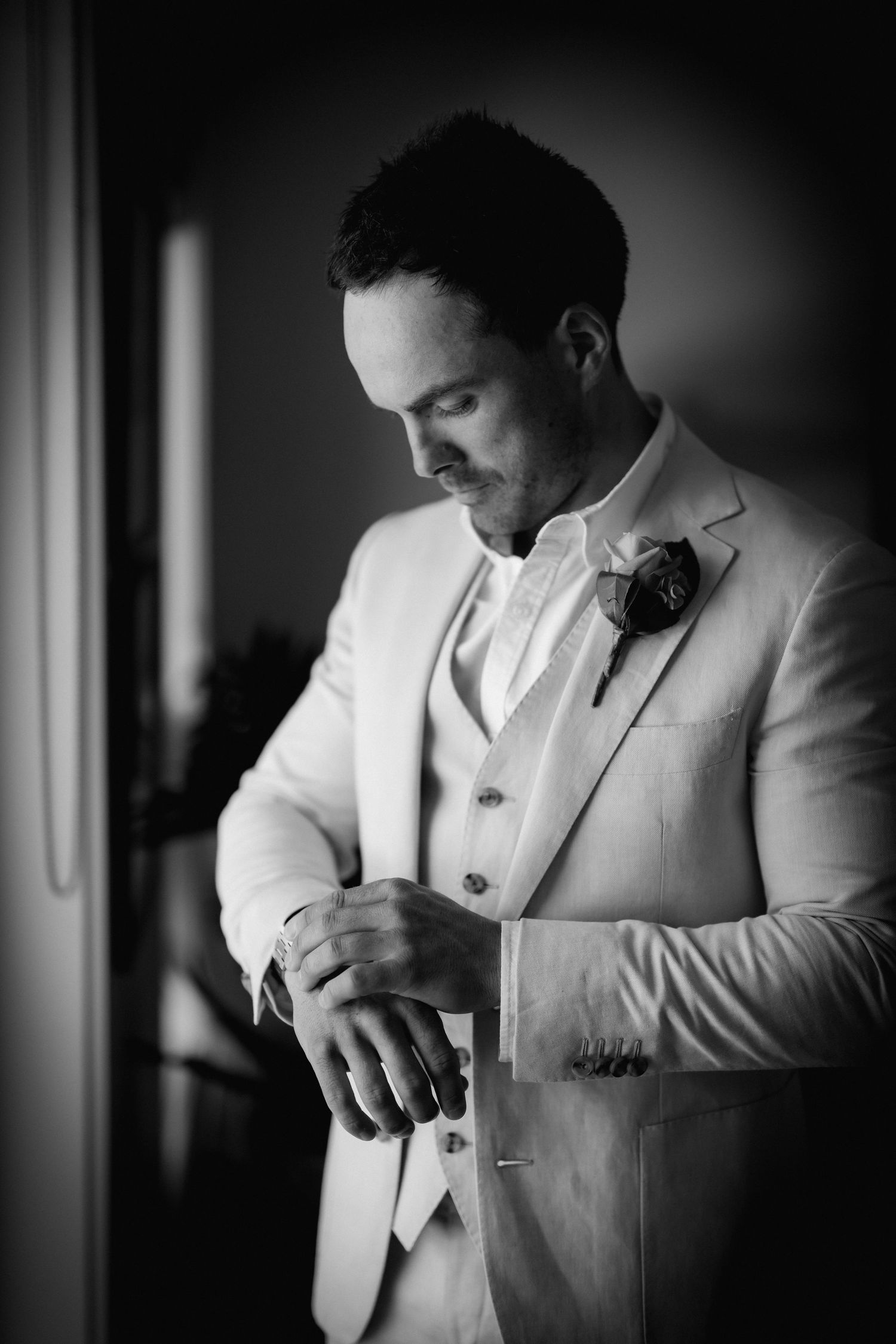 Close-up black and white photos show a groom adjusting his white suit jacket and tie before the ceremony.