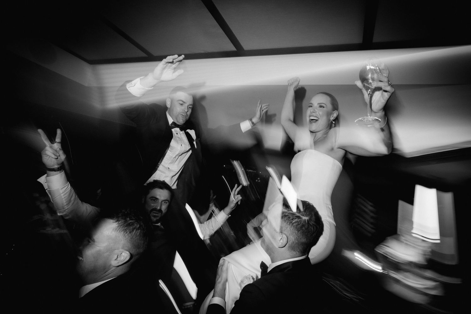 Black and white photo showing celebratory dancing and jumping at a wedding reception.