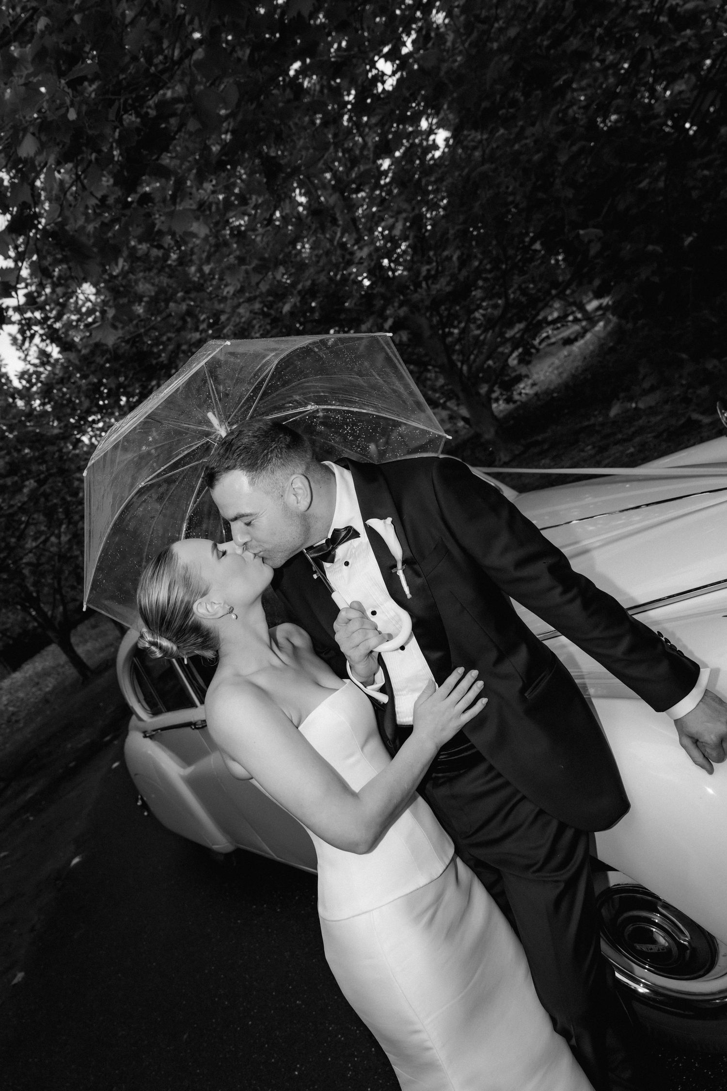 Romantic wedding photo with couple embracing near classic car under veil.