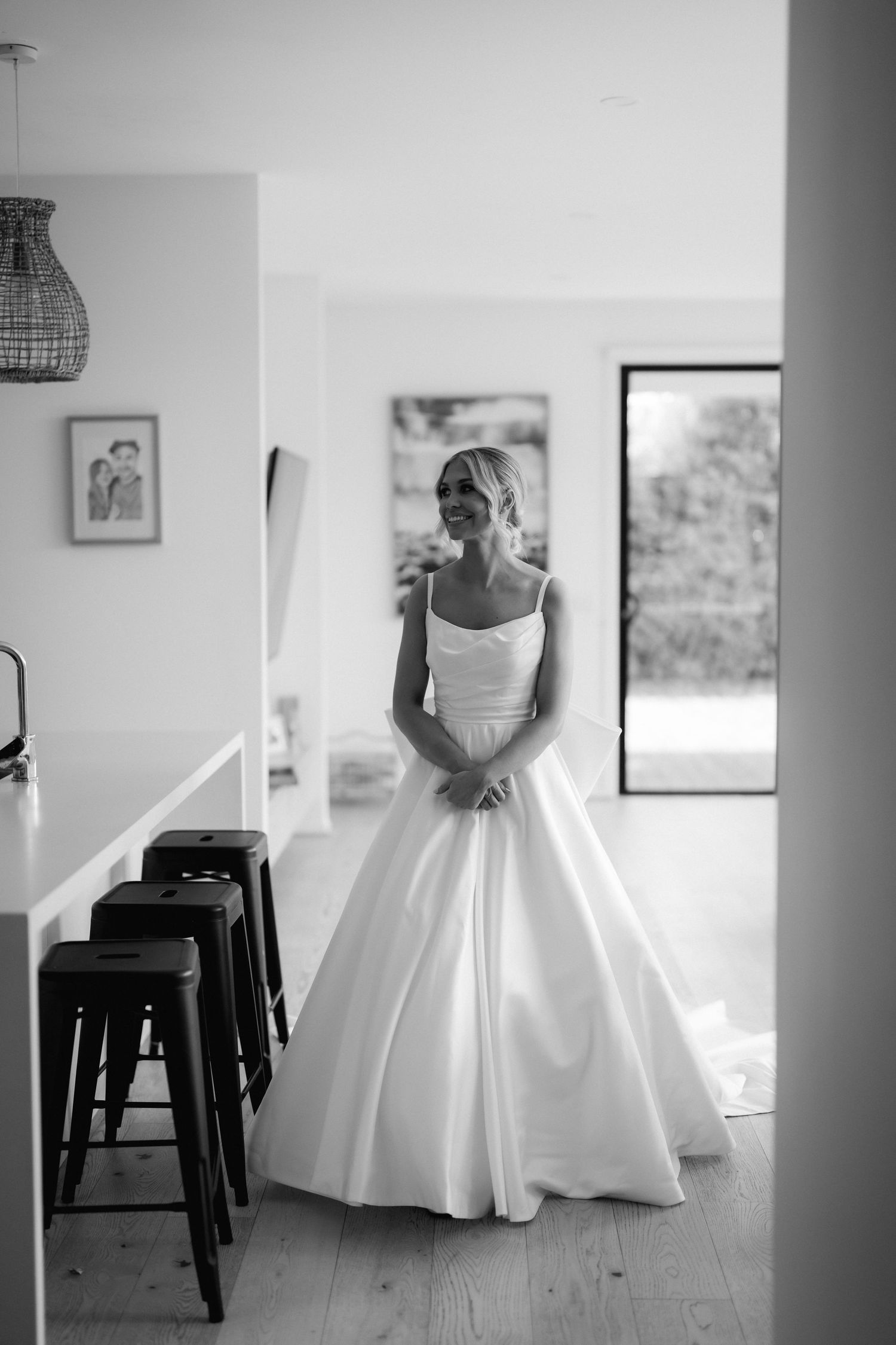 Elegant bride in minimalist white ballgown standing in modern interior with industrial bar stools.