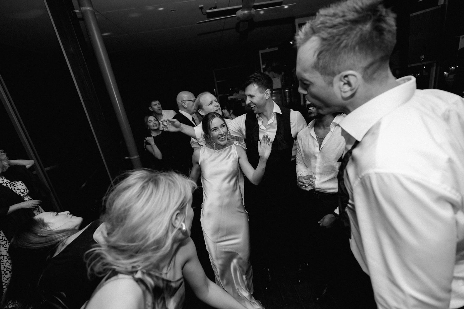 Wedding guests dancing and celebrating together on a dark dance floor during a lively reception party.