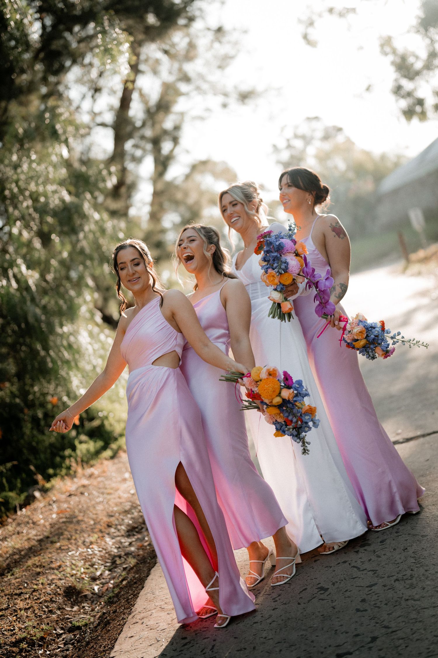 Bridesmaids in pink dresses walking together with vibrant colorful bouquets on a sunny path.