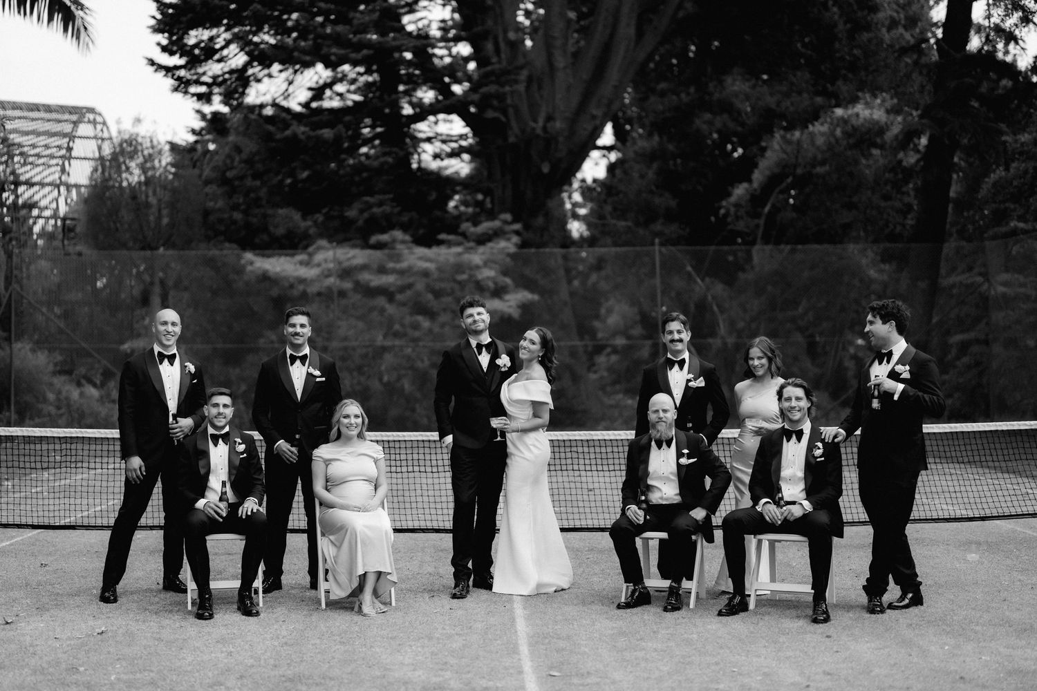 A classic black and white wedding party portrait taken outdoors with formal attire and elegant composition.