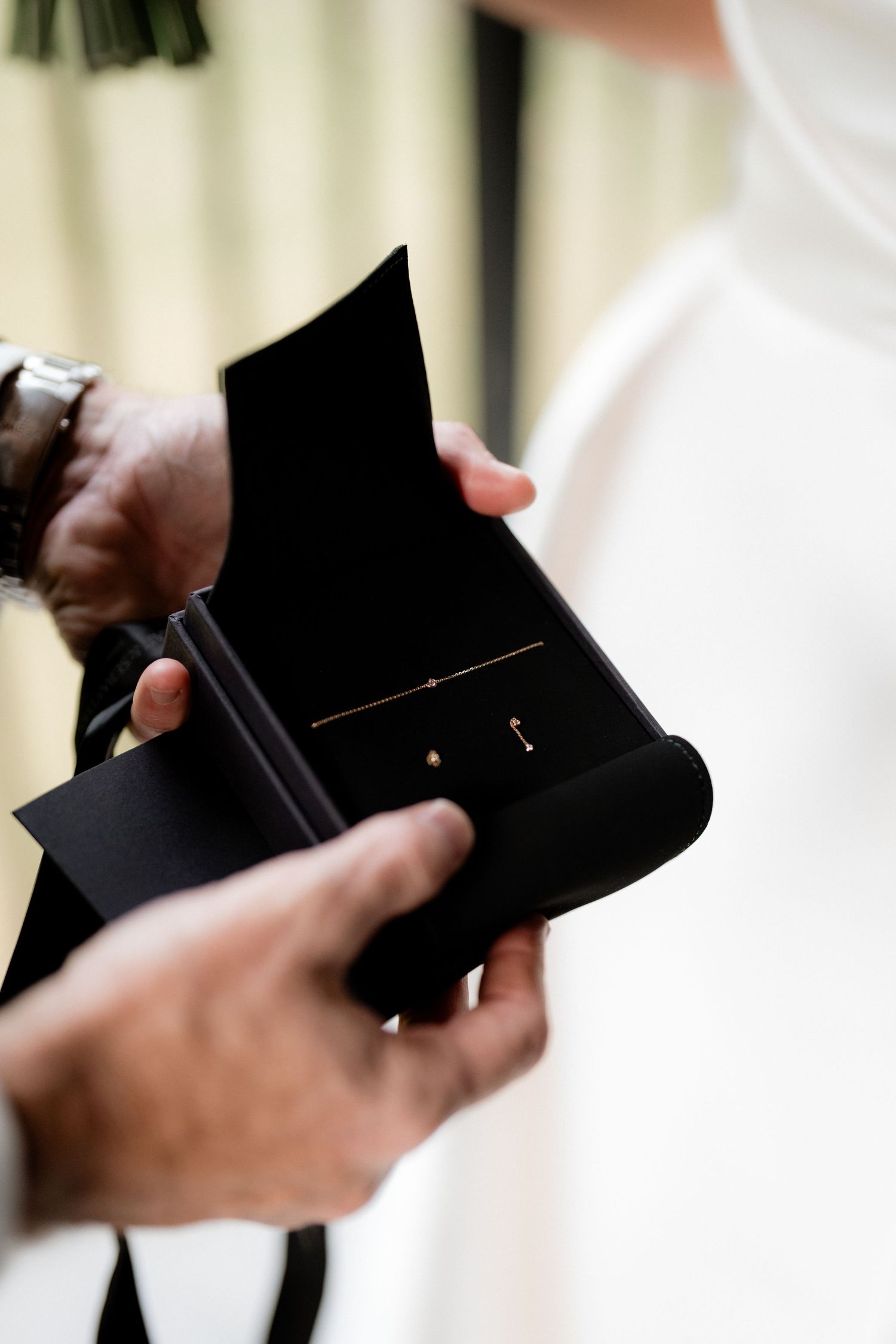 Close-up shot of hands holding an open black ring box during a wedding ceremony.