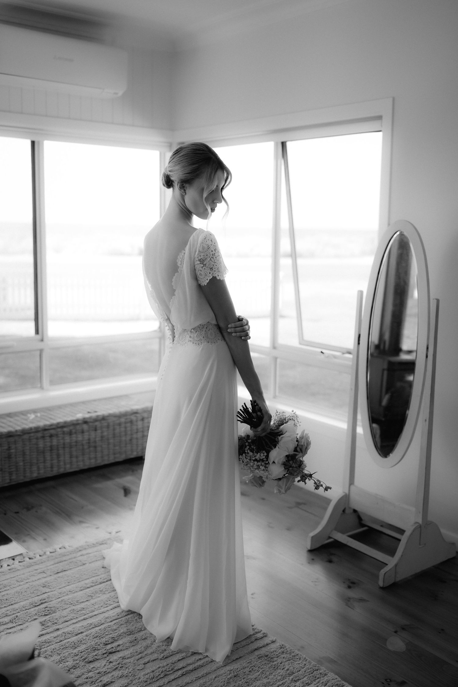 Elegant wedding dress with open back and lace details shown in black and white against bright windows.