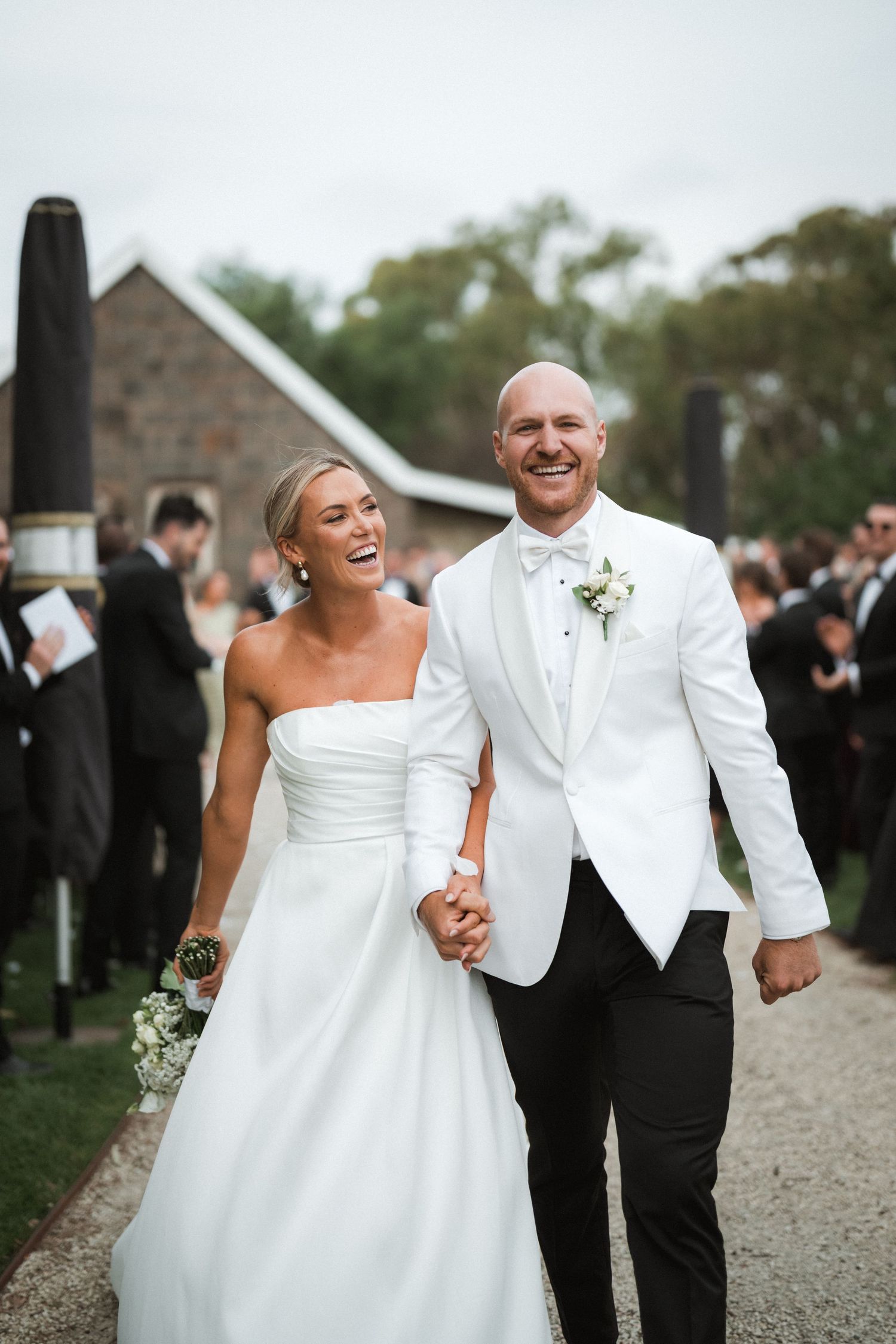Happy newlyweds share a joyful candid moment walking together after their outdoor wedding ceremony.