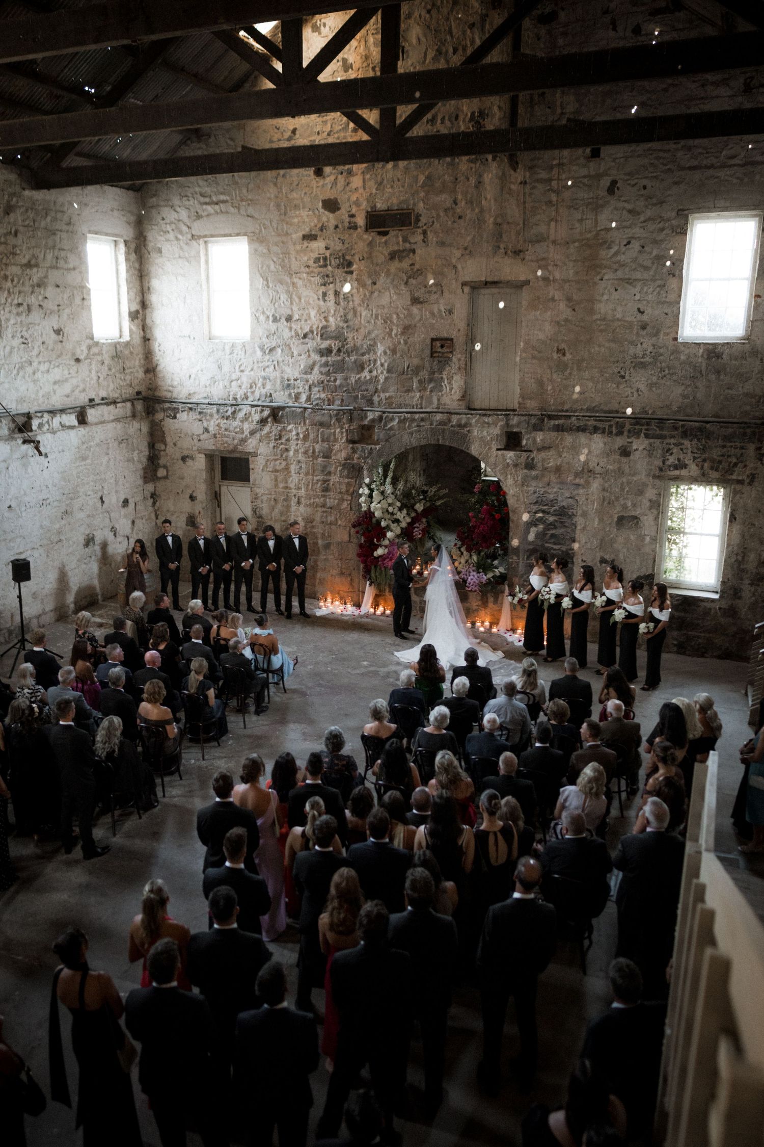 Wedding ceremony taking place in a rustic stone barn venue with exposed brick walls and natural light streaming through windows.