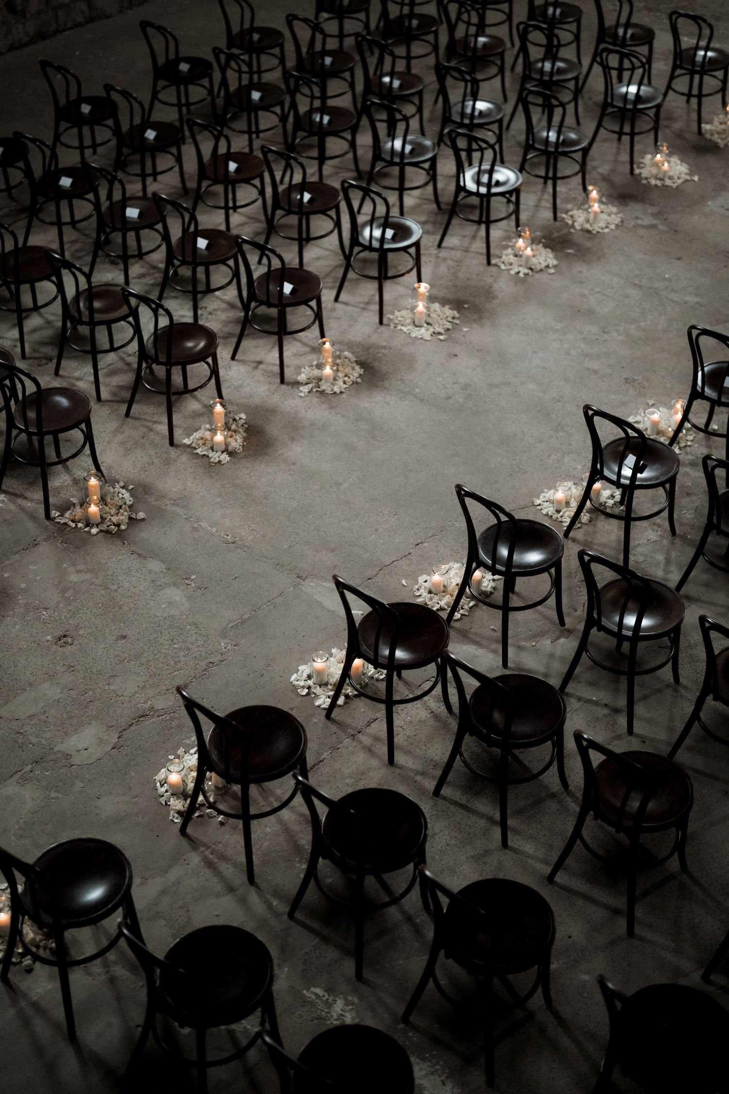 Rows of empty black chairs arranged with small candlelit decorations creating a moody wedding ceremony setting.