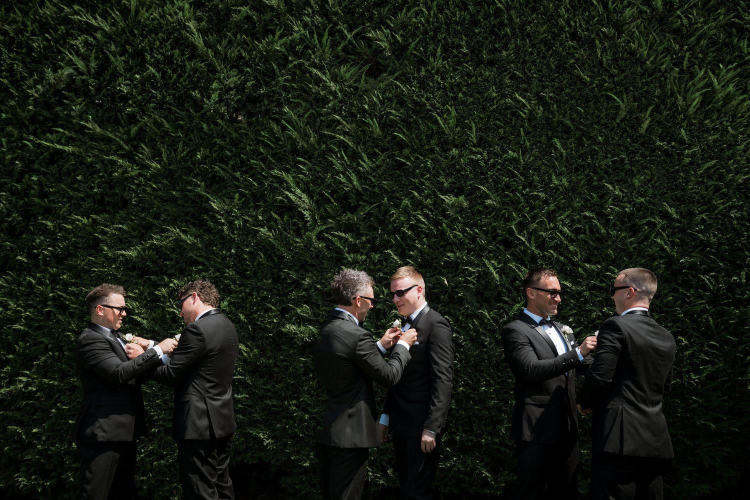 A sequence of playful groomsmen in black suits posing against a dark background.