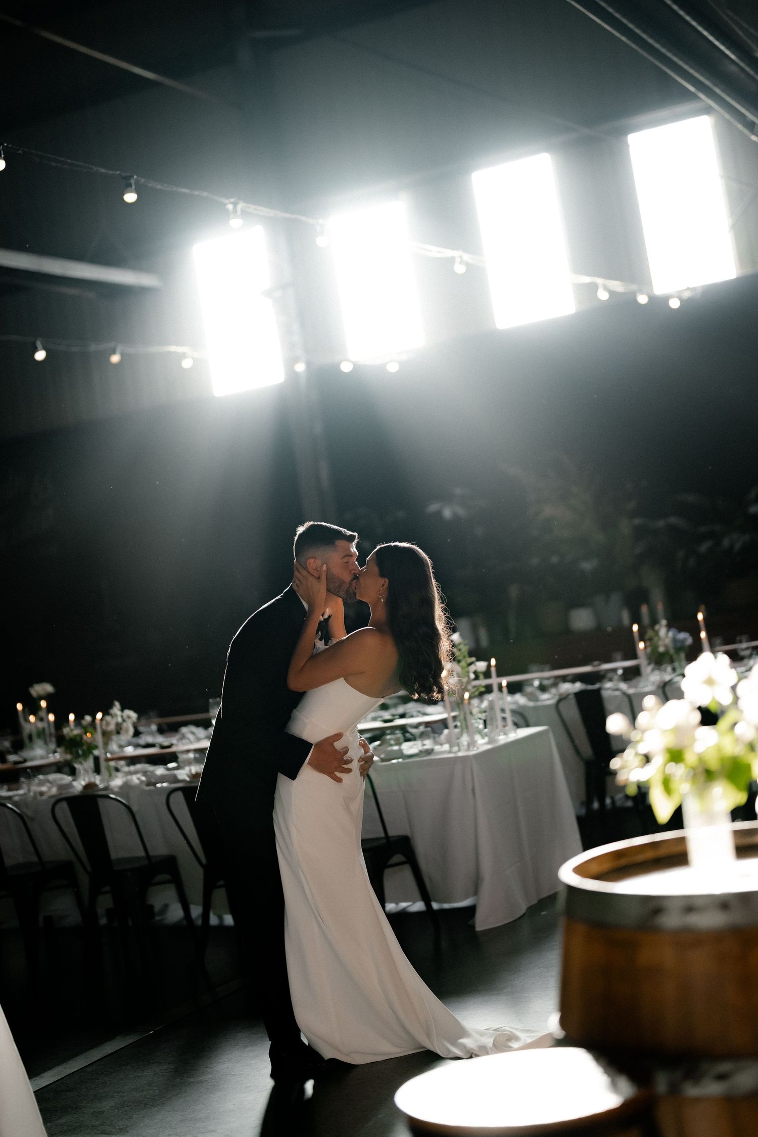 Dramatic silhouettes of a wedding couple dancing in a reception venue with bright window backlighting.