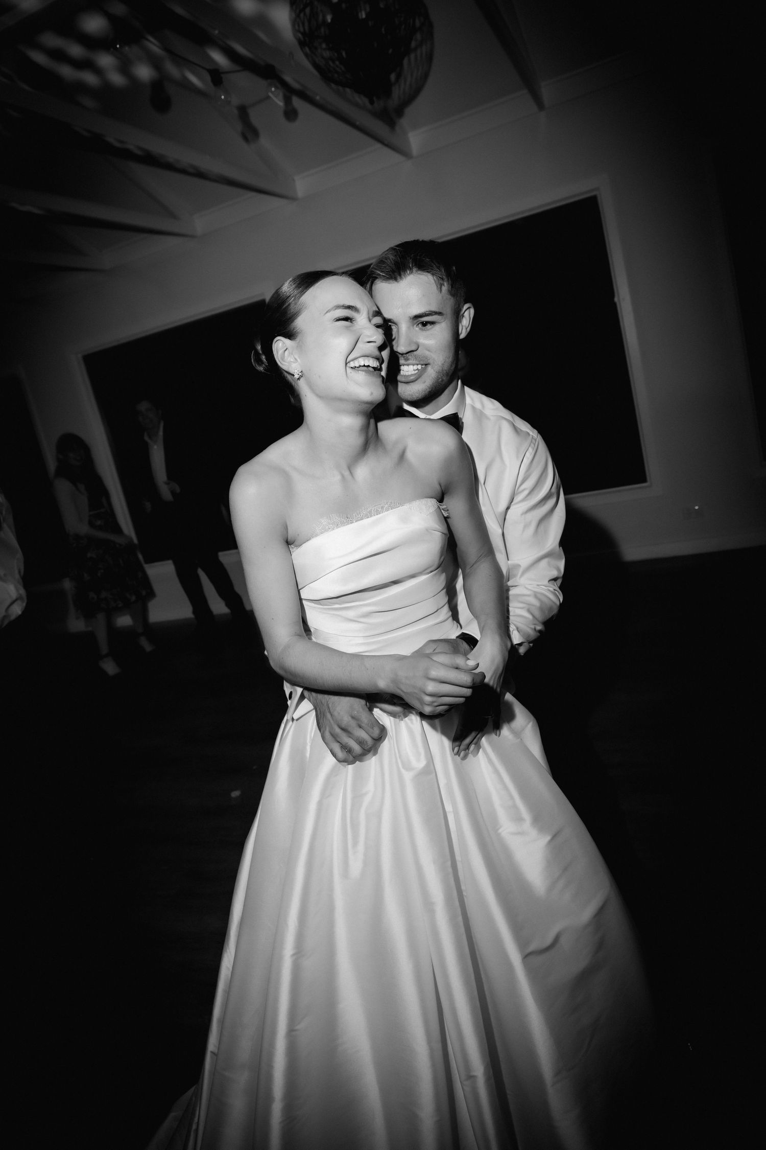 A couple shares an intimate dance moment in dramatic black and white lighting.