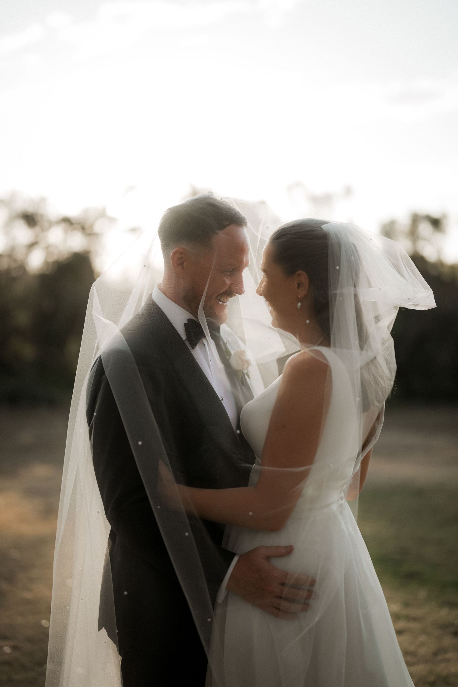 Romantic wedding portrait silhouetted against golden sunset light with flowing veil.