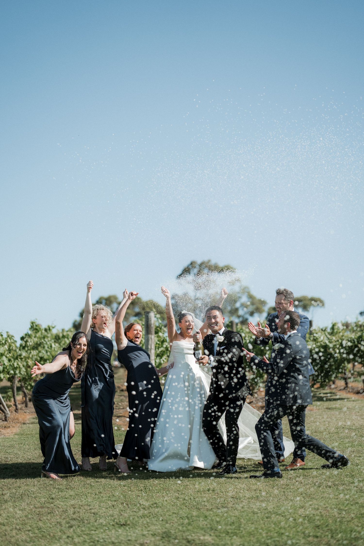 Wedding party throws confetti in celebration on a sunny day with blue skies.