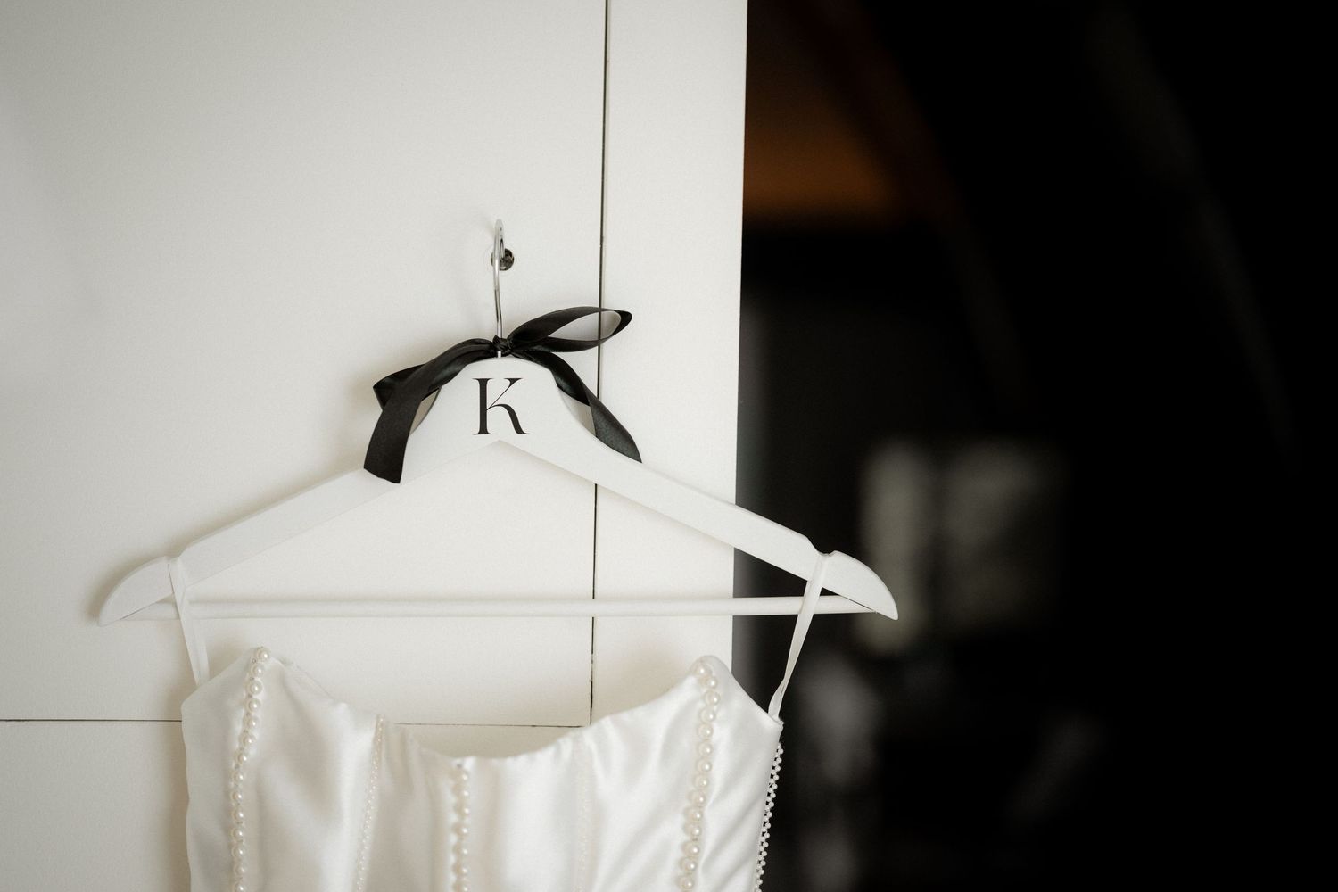 White wedding dress hangs on a personalized hanger against a light wall.