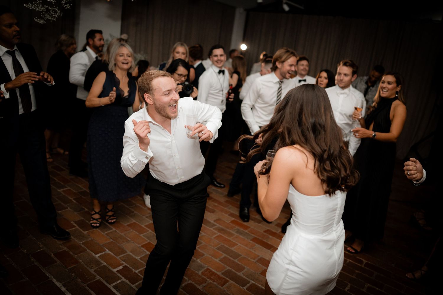 Wedding party dancing energetically on a wooden dance floor during reception celebrations.